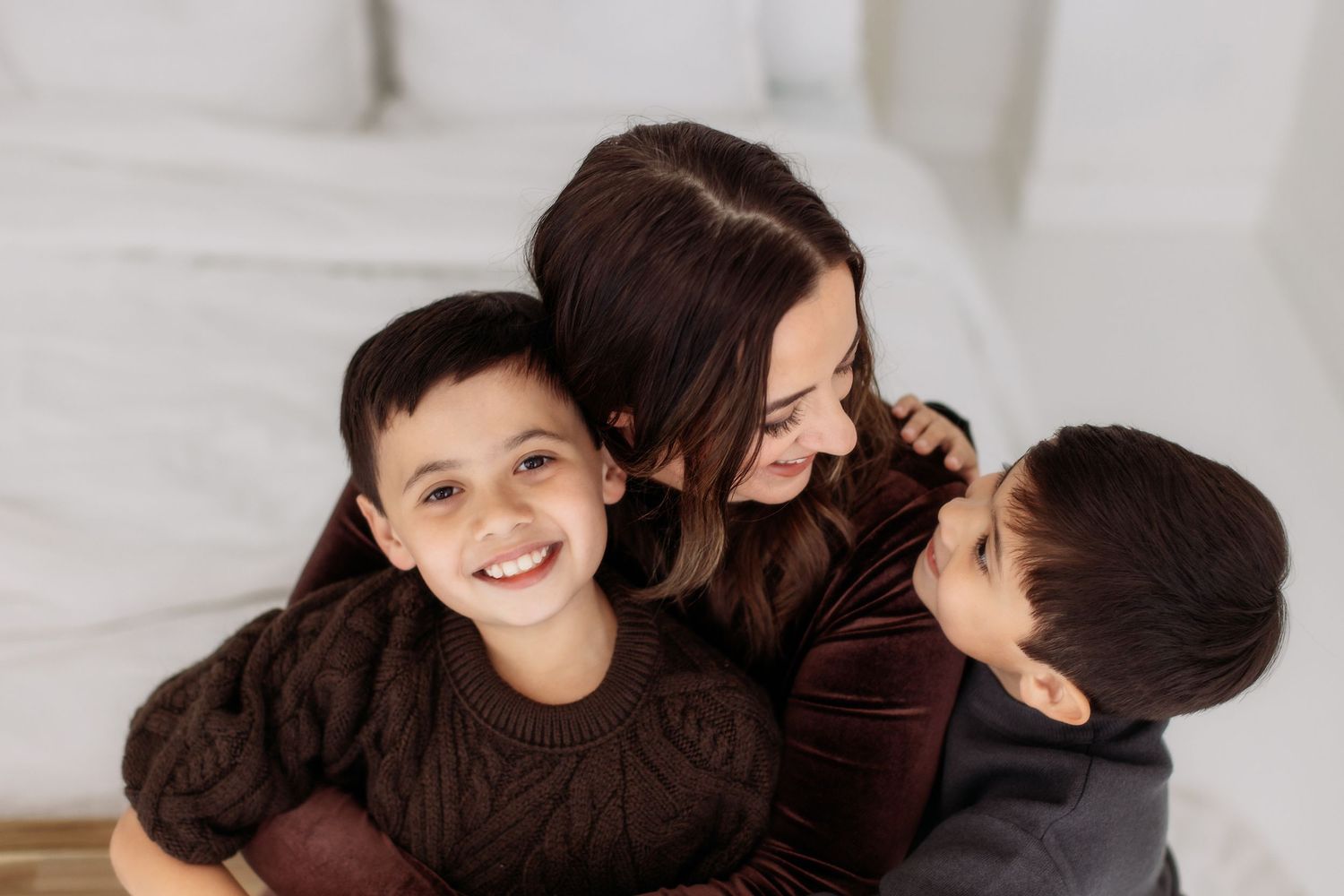 A loving moment shared between mother and children wearing brown sweaters on a white couch.