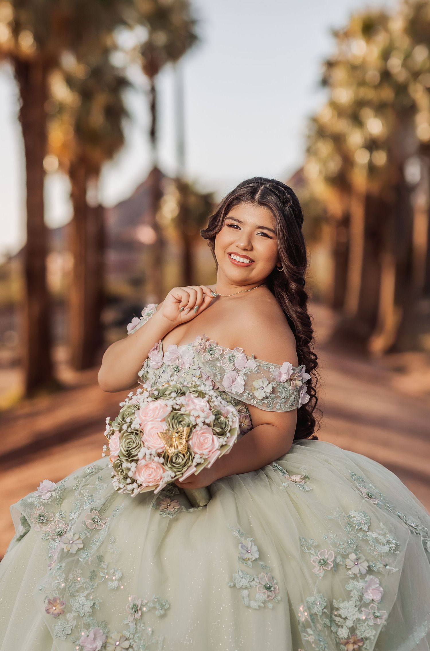 Floral green quinceanera gown sparkles in golden sunset light among palm trees in elegant portrait photoshoot.