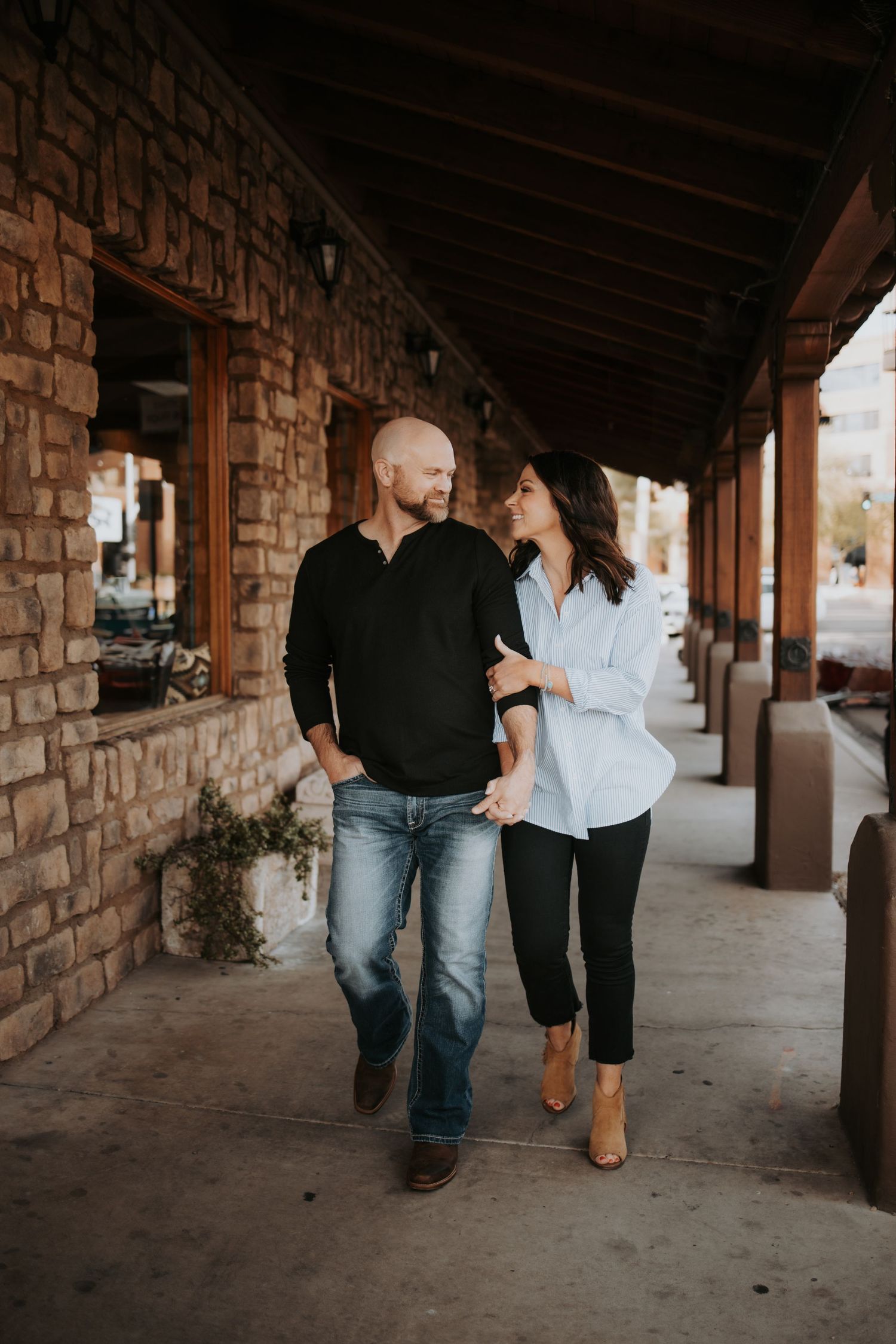 A couple walking together under a covered brick walkway with rustic architecture and warm autumn lighting.