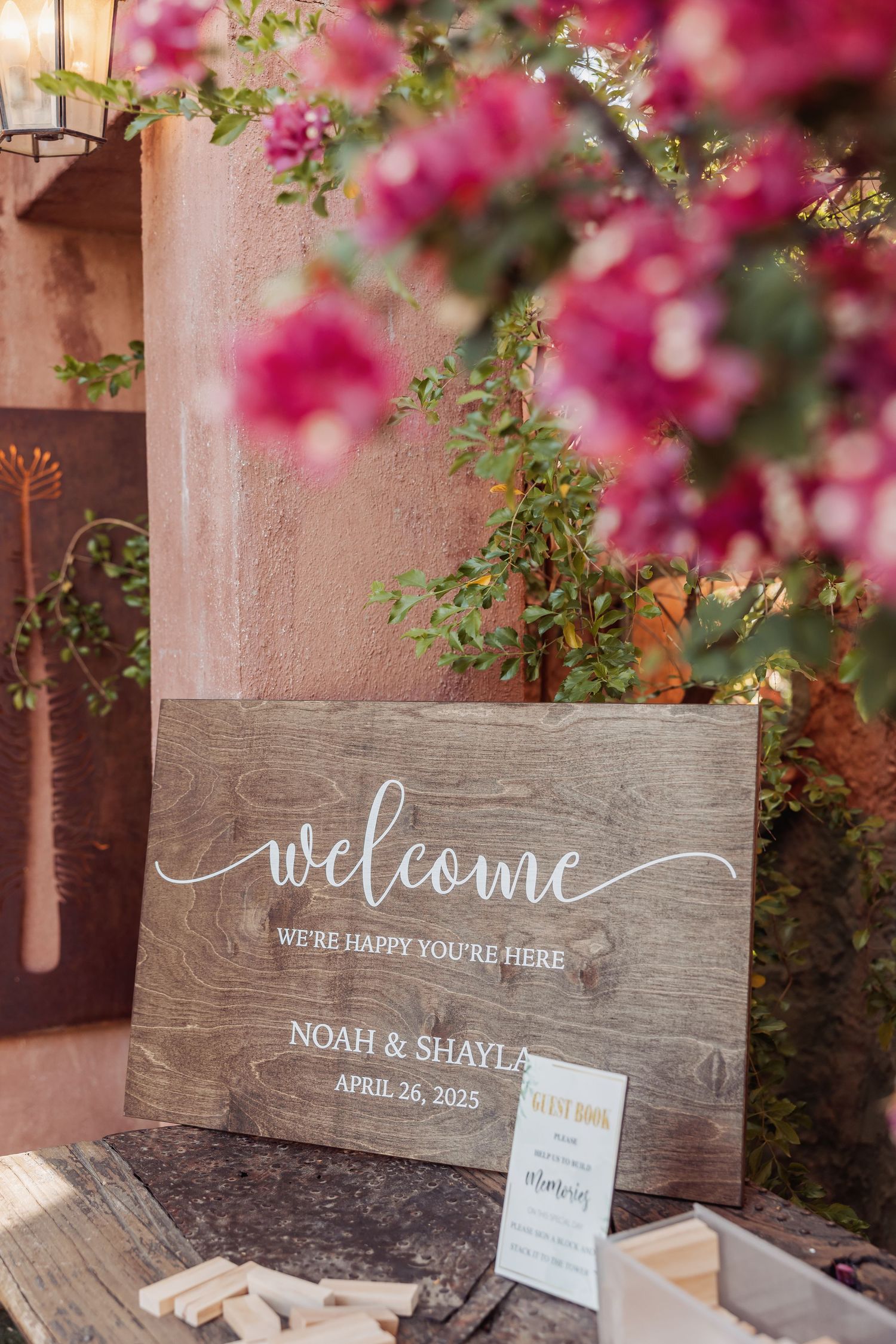 Rustic wooden wedding welcome signs with white calligraphy displayed among pink bougainvillea flowers.