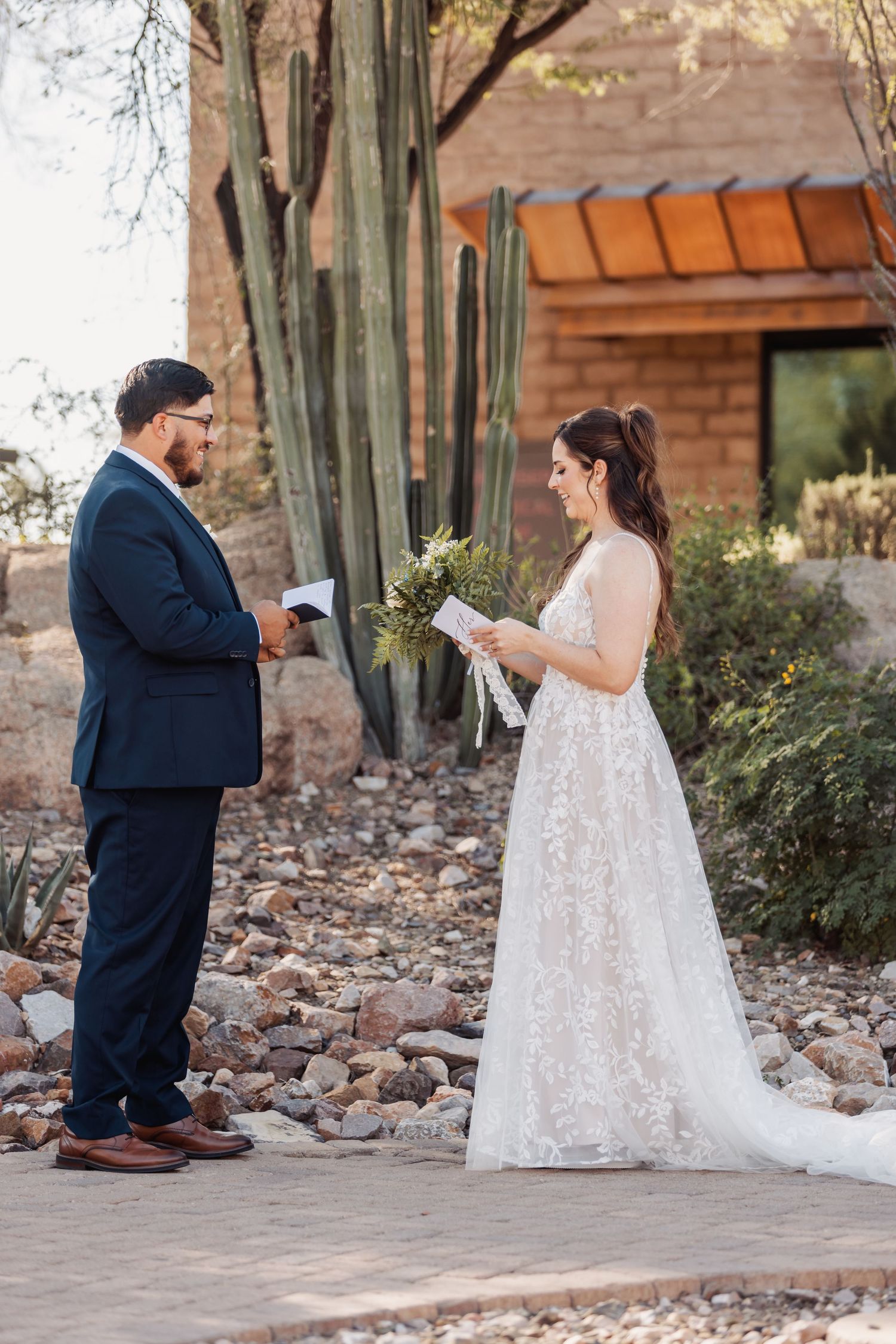 Couple reading personal vows to each other on a brick pathway with saguaro cacti in the background.