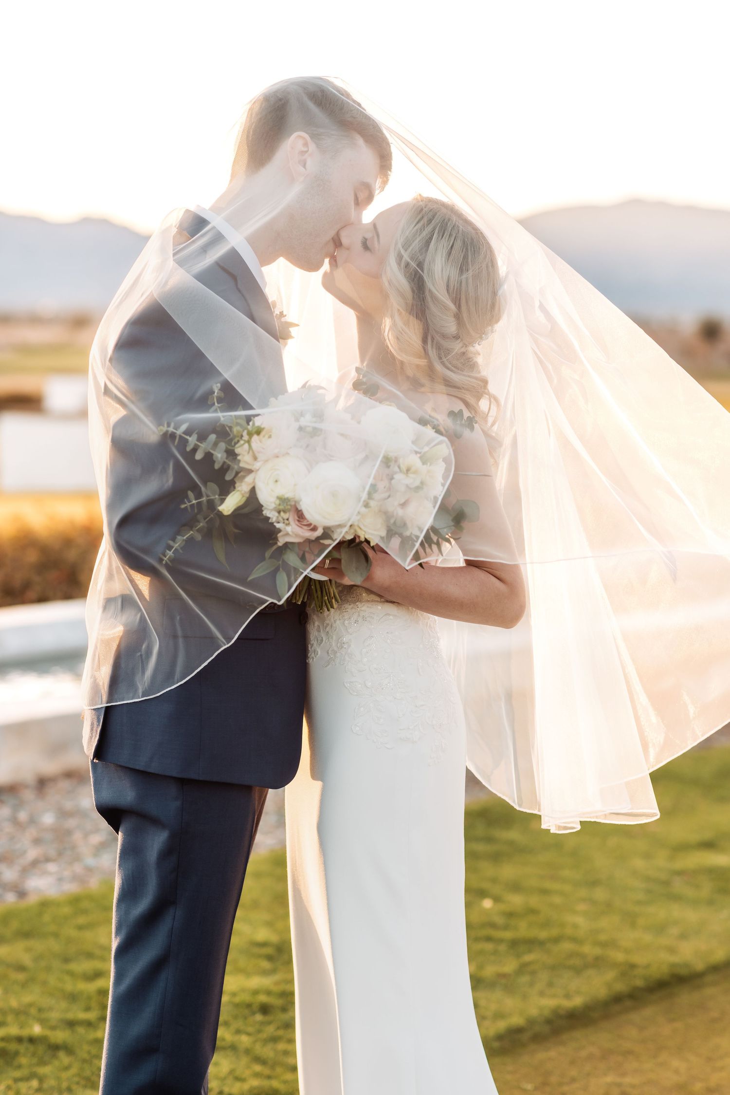 Romantic sunset wedding portrait with flowing veil catching golden light in an outdoor setting.