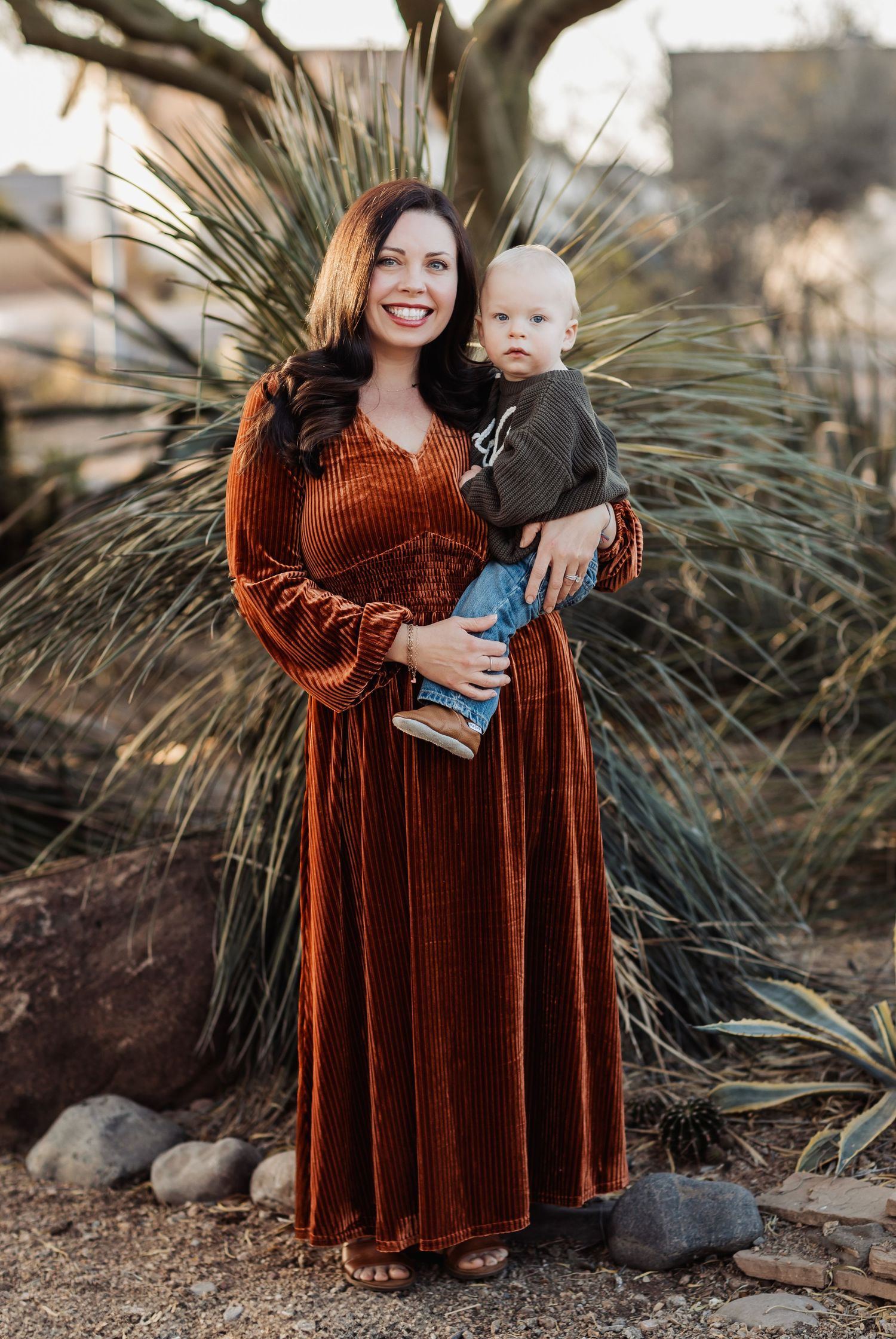 Outdoor portrait against desert plants showing a rust-colored velvet maxi dress in warm sunlight.
