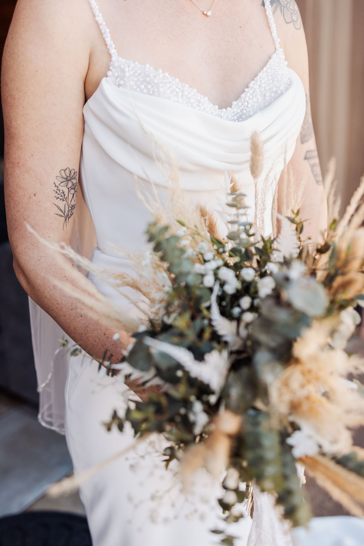 Detailed shot of a bridal bouquet with dried flowers and greenery against a white wedding dress.