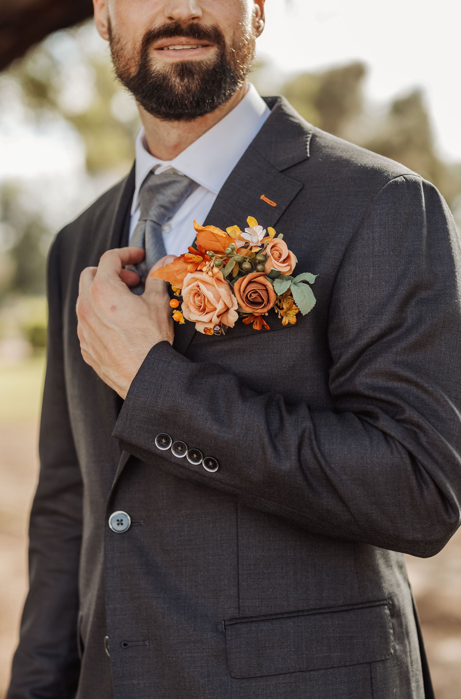 Wedding party members in dark suits with orange floral boutonnieres adjust their ties and lapels.