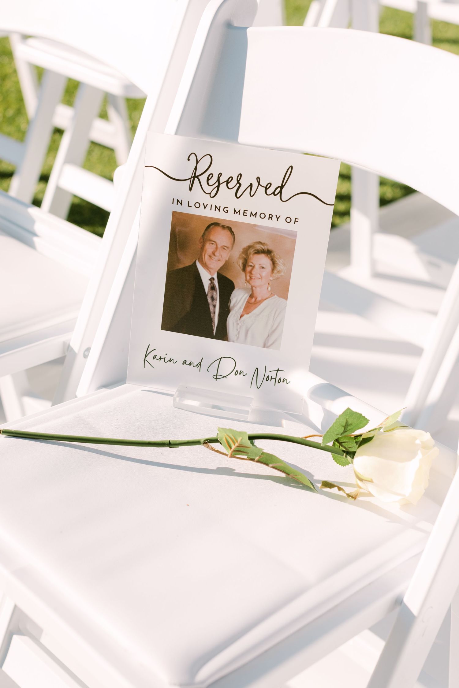 White wedding ceremony chairs with reserved signs and floral decorations set up outdoors.