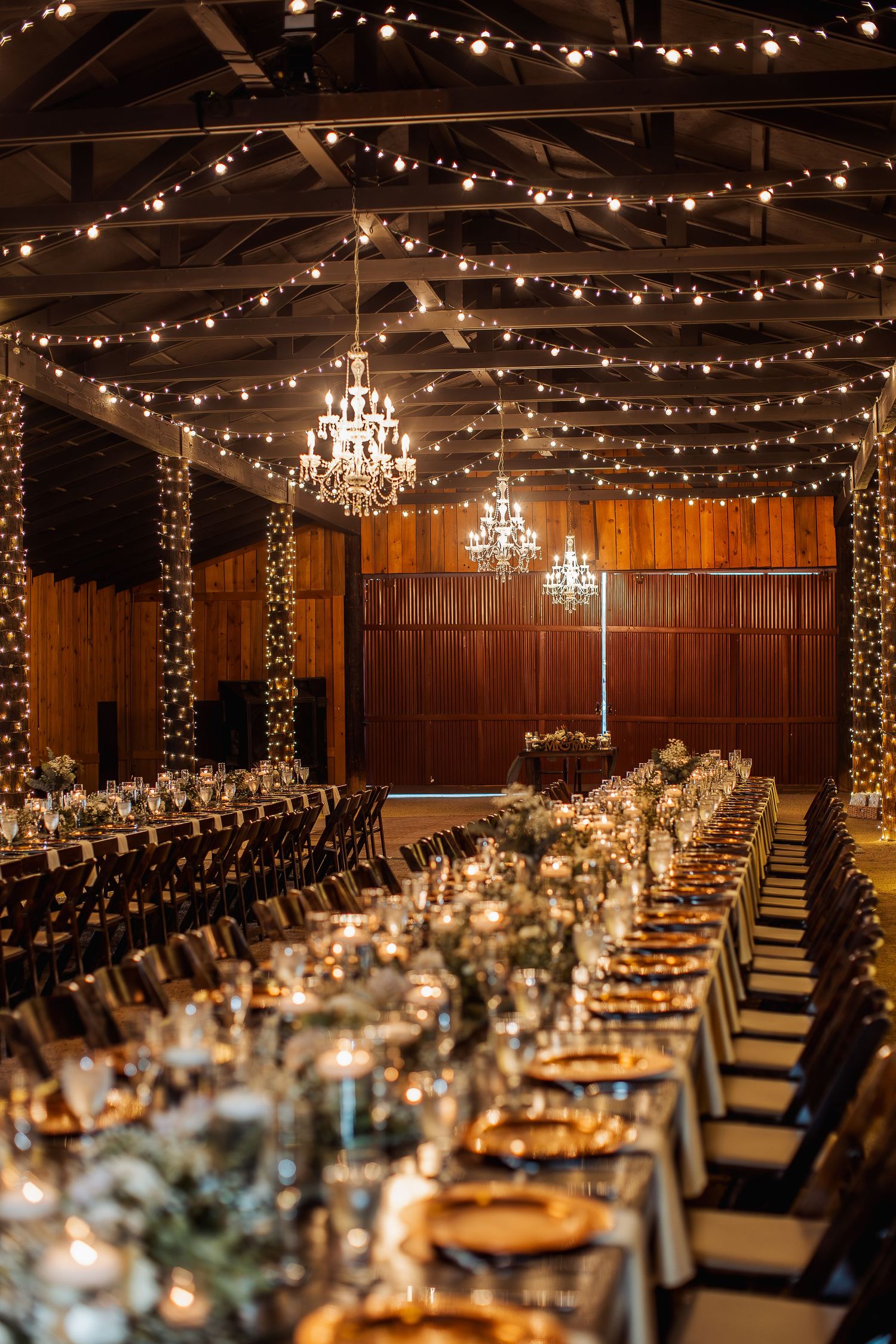 Elegant wedding reception venue with wooden walls, string lights, chandeliers and long banquet tables.
