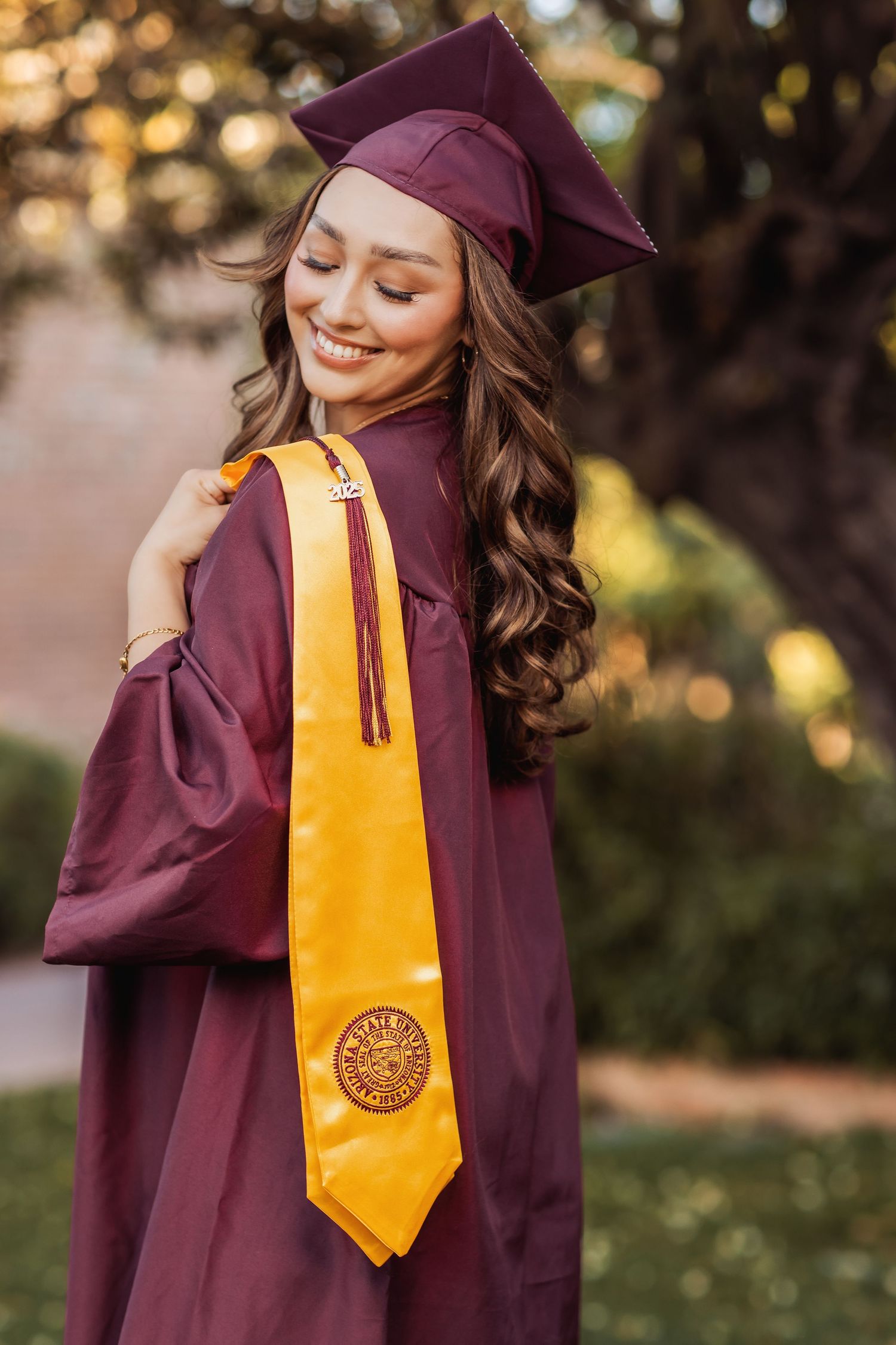 Graduate wearing maroon cap and gown with gold honors stole poses outdoors for graduation photos.