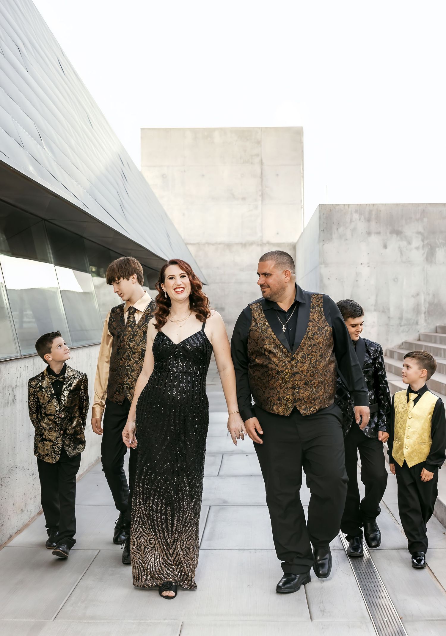 Wedding party members in black and gold attire walk together along a modern architectural walkway.