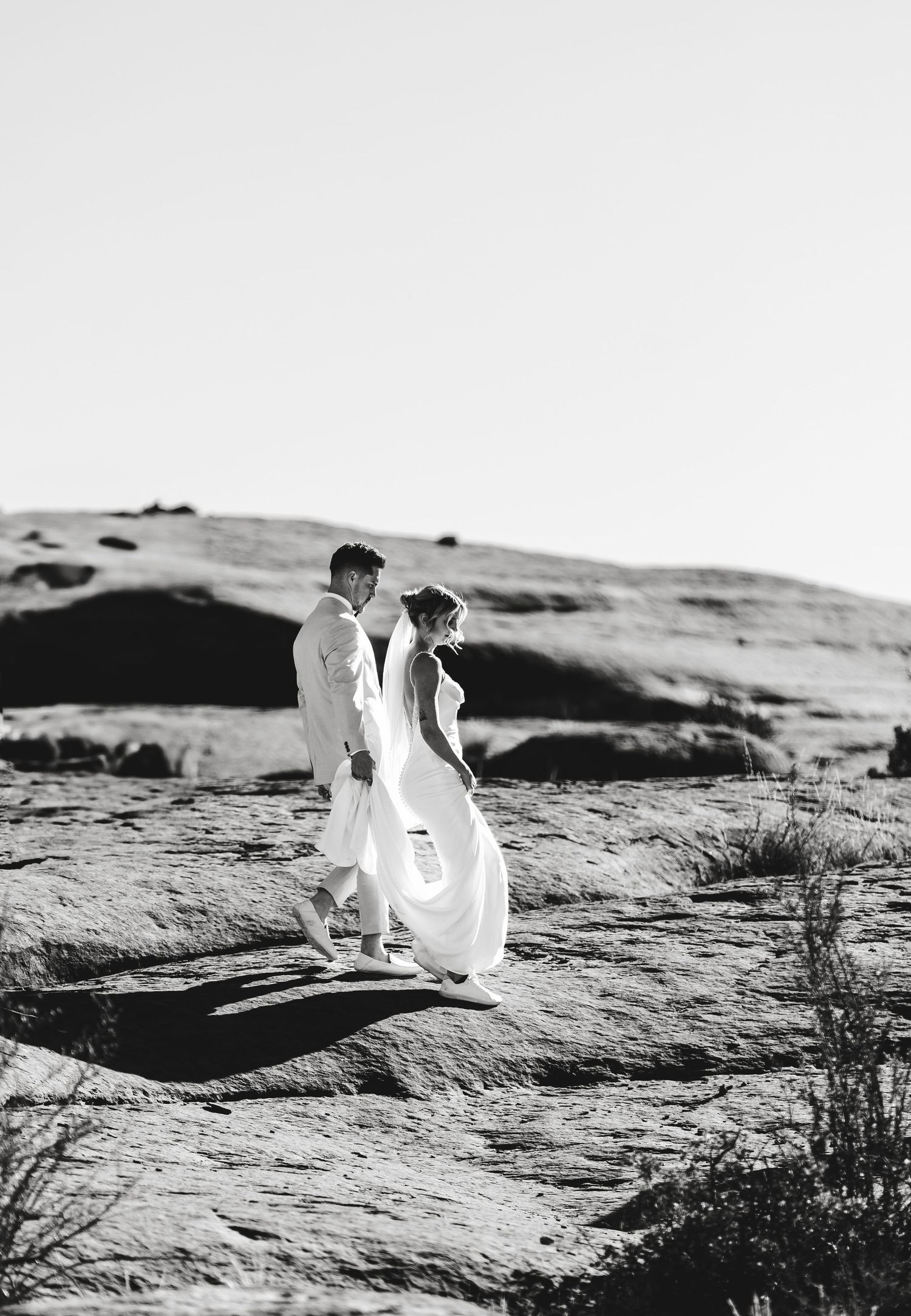 A romantic black and white landscape view shows two figures walking along rocky desert terrain at sunset.