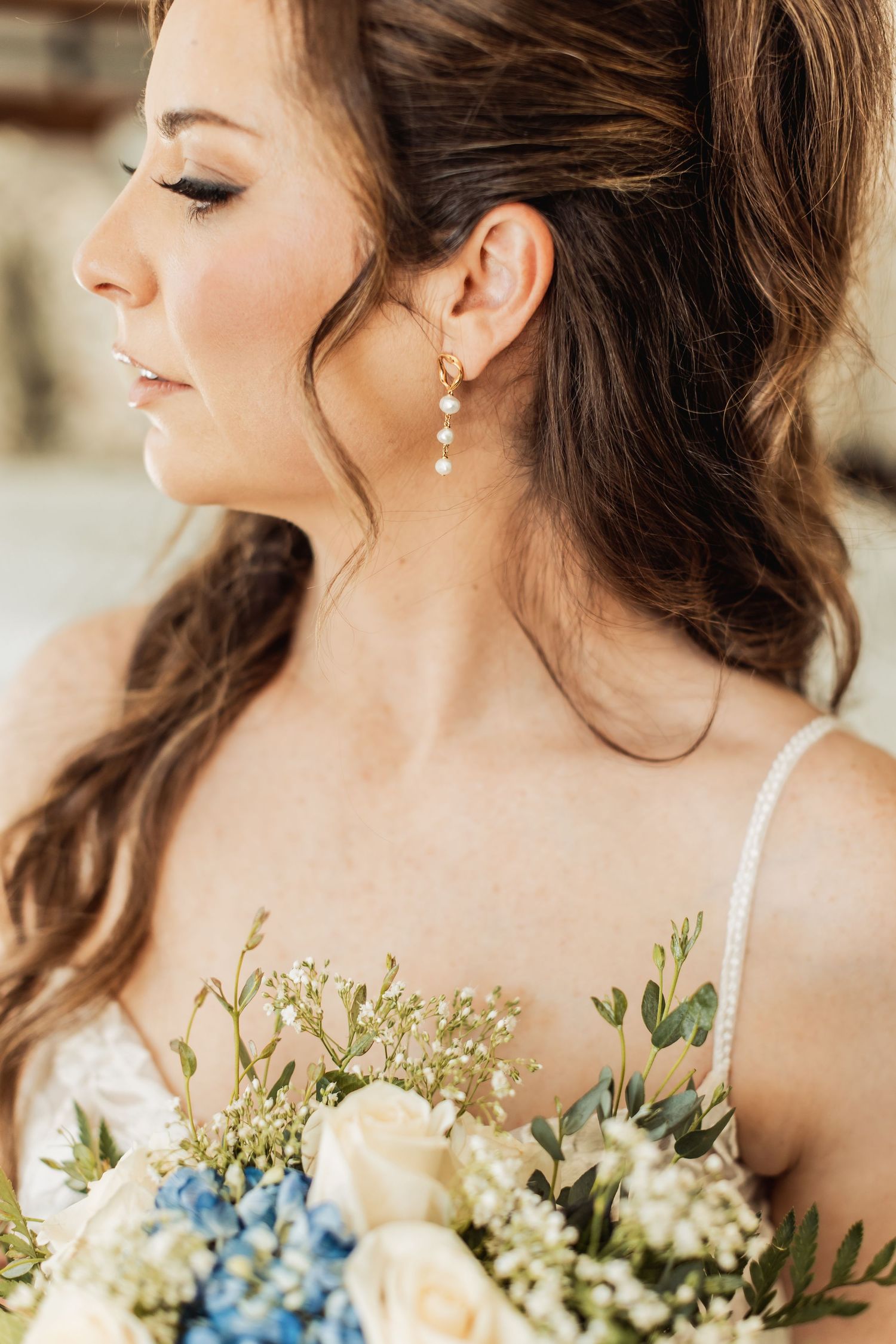 Elegant bridal portrait series featuring delicate pearl earrings and a romantic bouquet with cream and blue flowers.