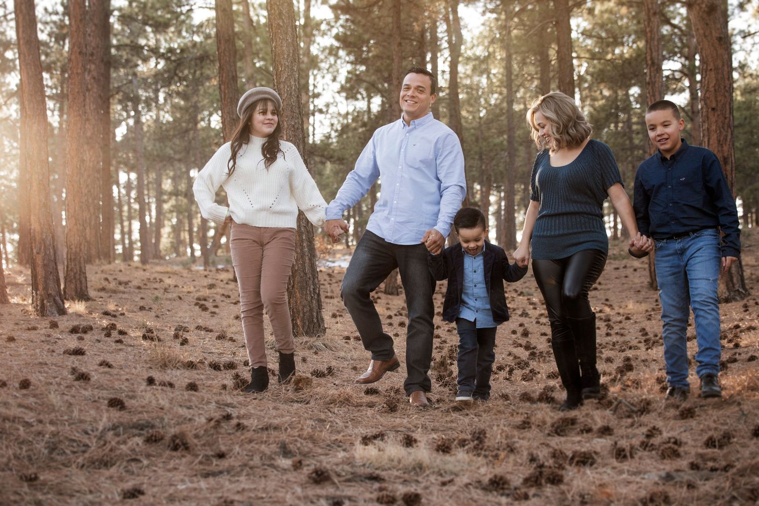A group of people walking together through a sunlit pine forest on rocky terrain during golden hour.