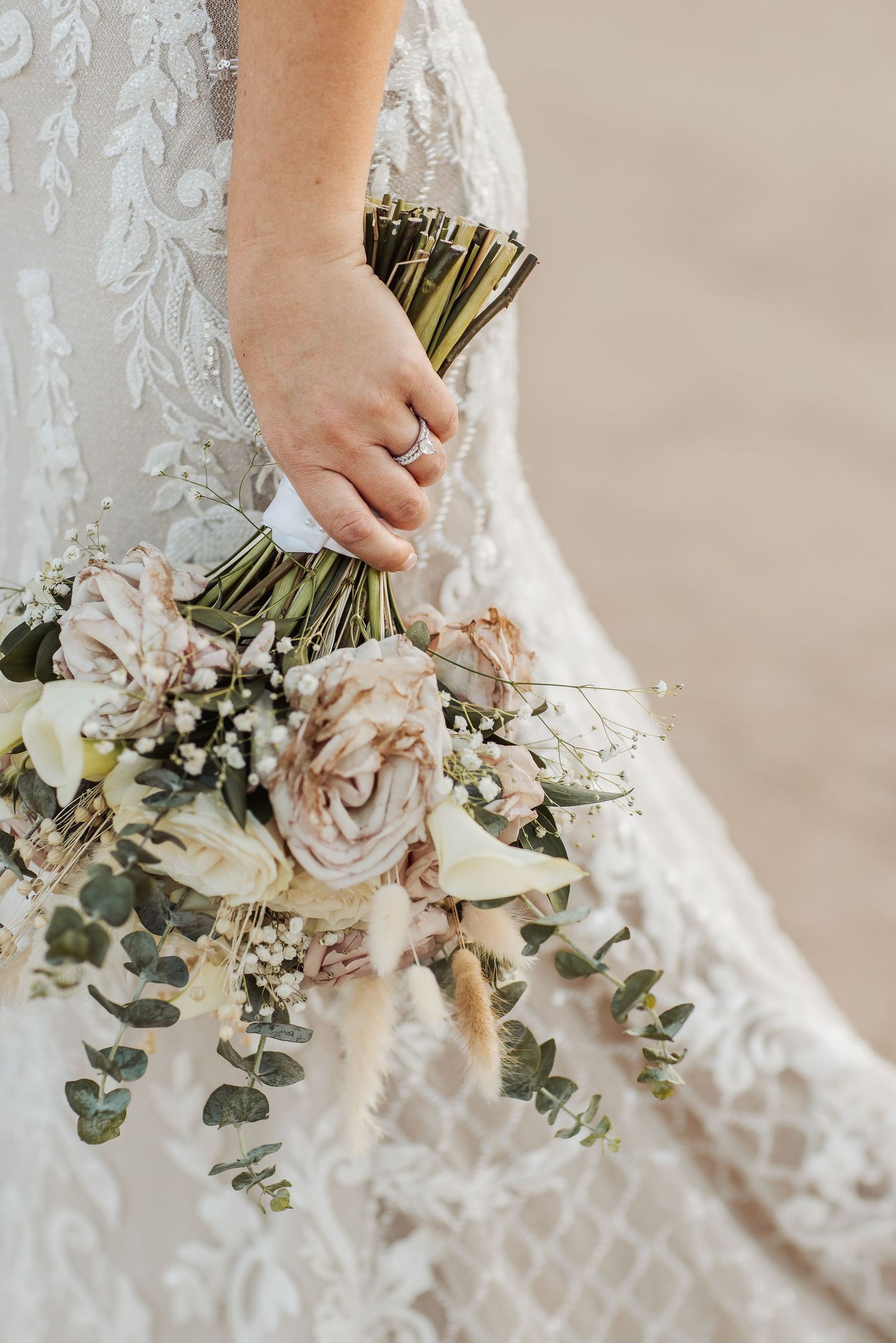 Close-up of a bridal bouquet with blush roses and eucalyptus against a detailed lace wedding dress.