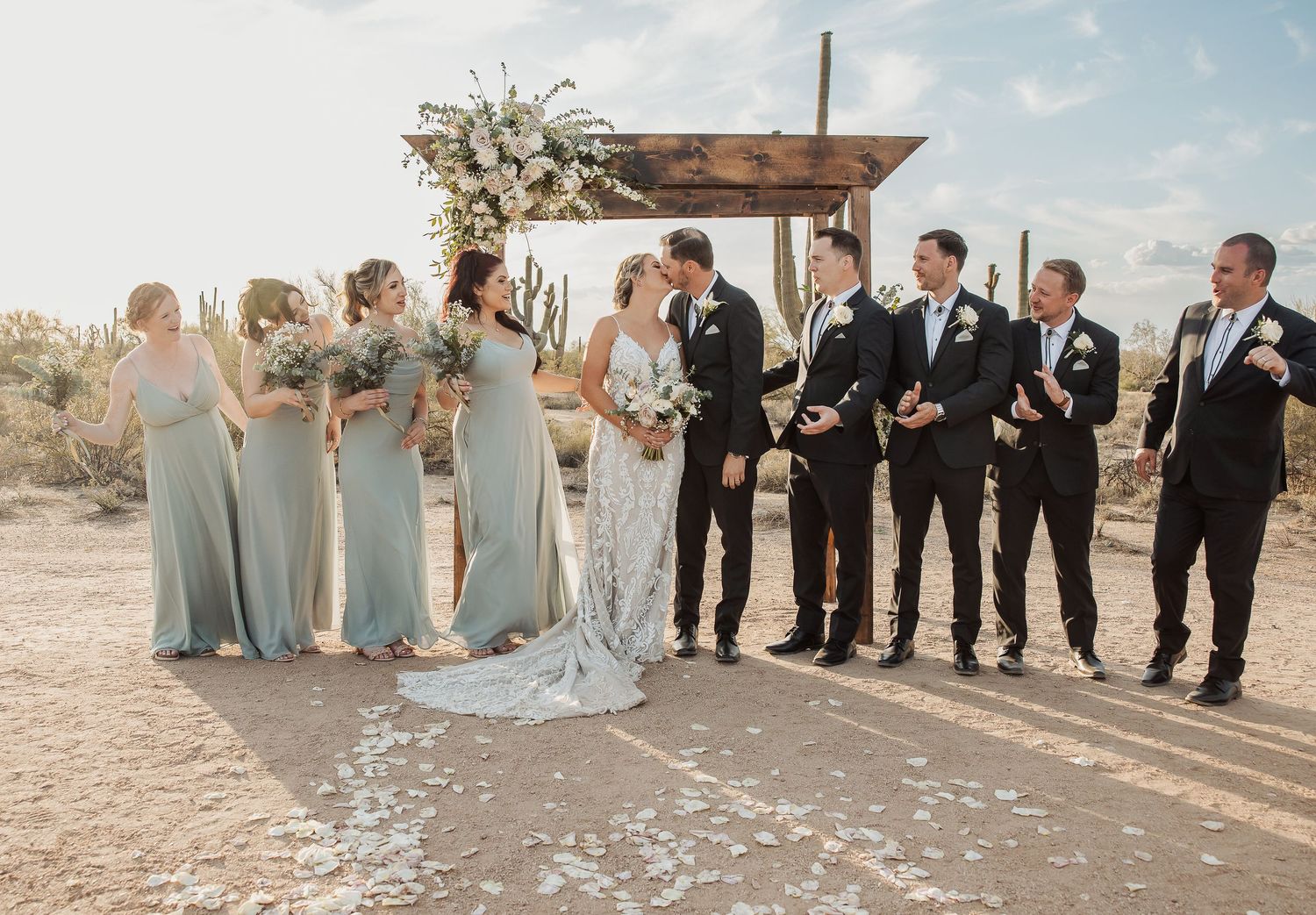 A wedding party poses together on a desert landscape in coordinated formal attire in muted blue and black tones.