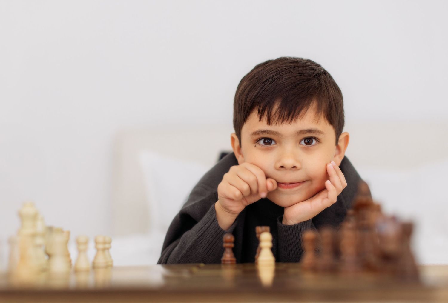 A young chess player contemplates their next move while sitting at a wooden chess board with pieces.