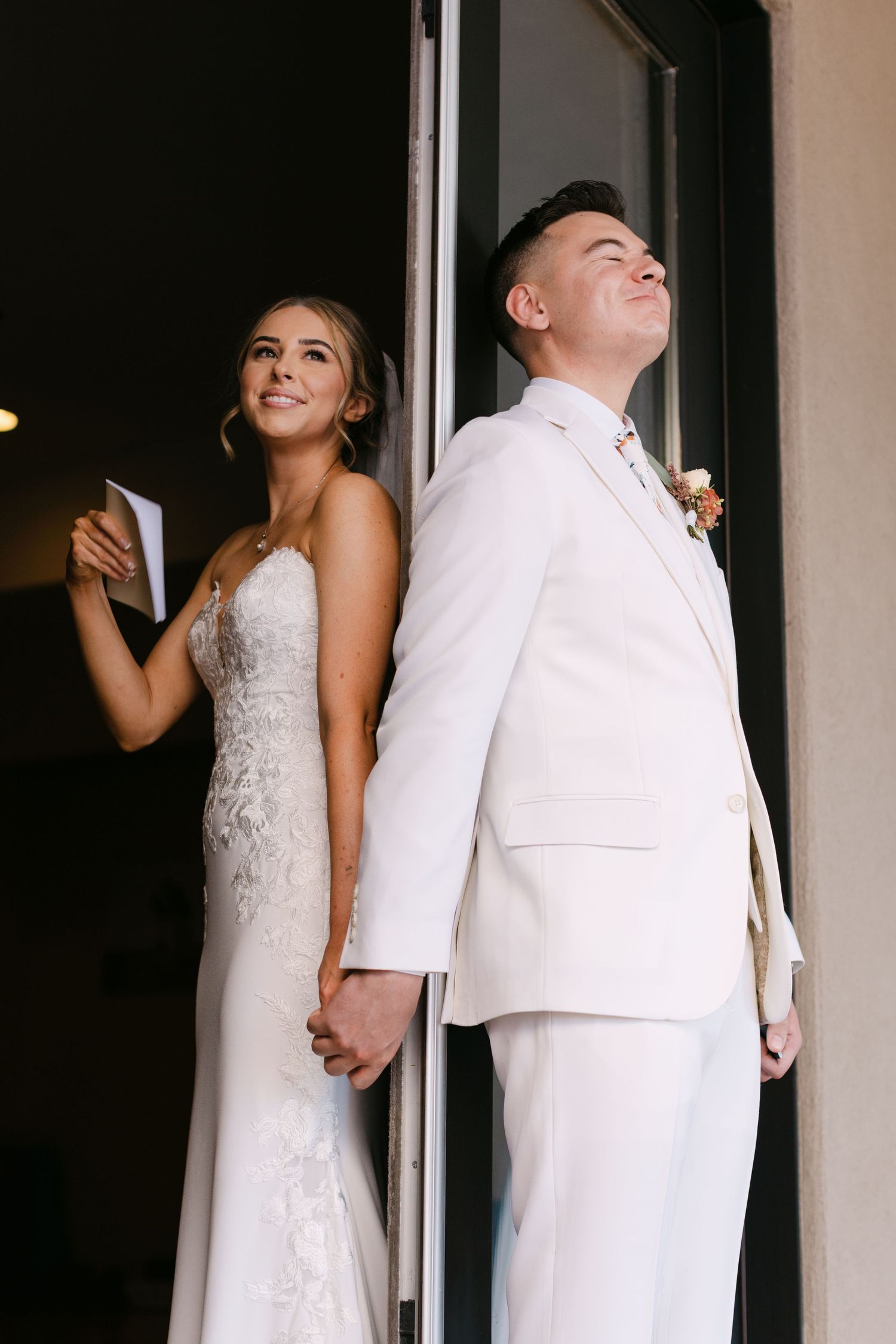 A couple in wedding attire stands back-to-back for a creative first look photo series.