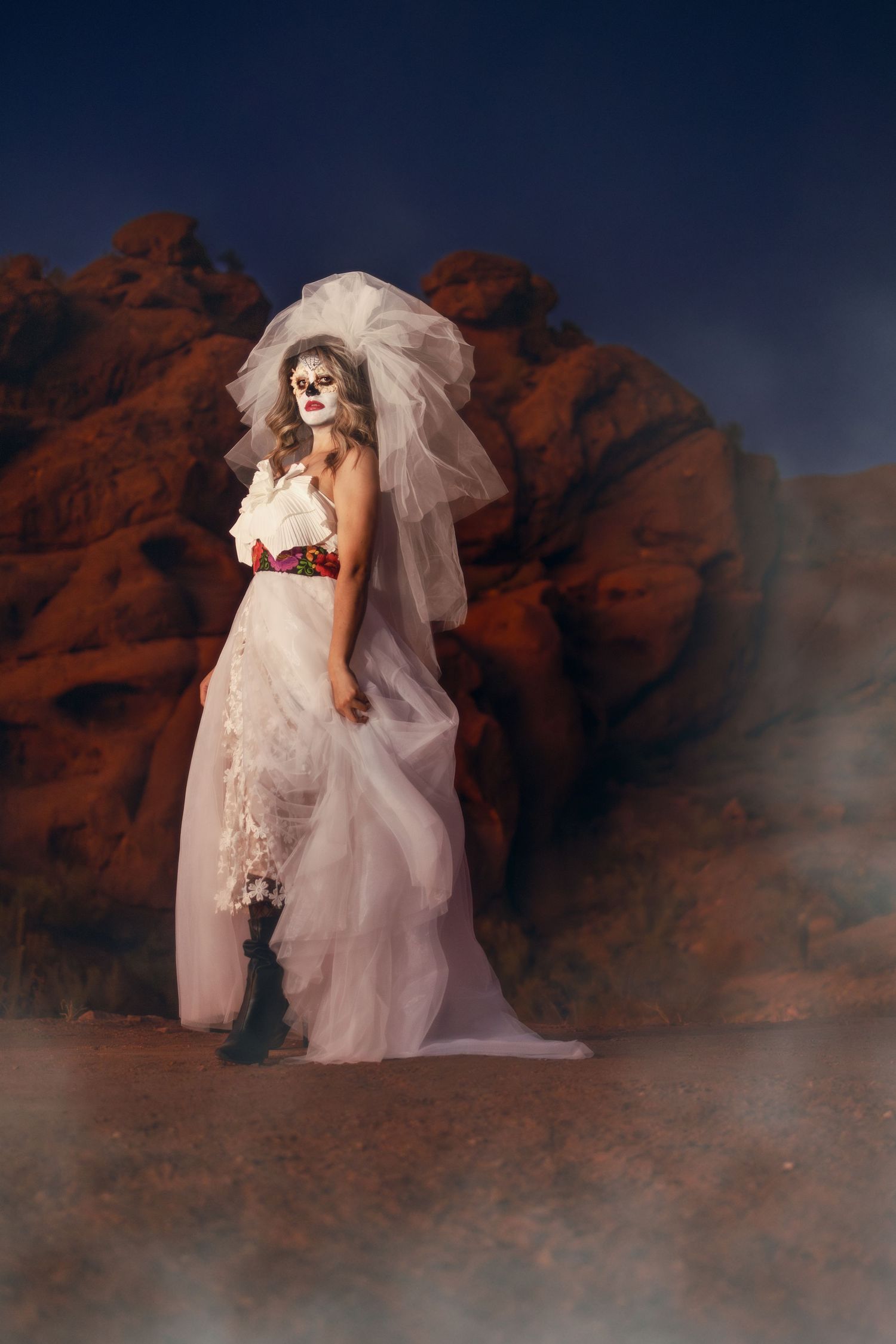 A bride in a flowing white gown and dramatic veil poses against red rock formations in atmospheric fog.