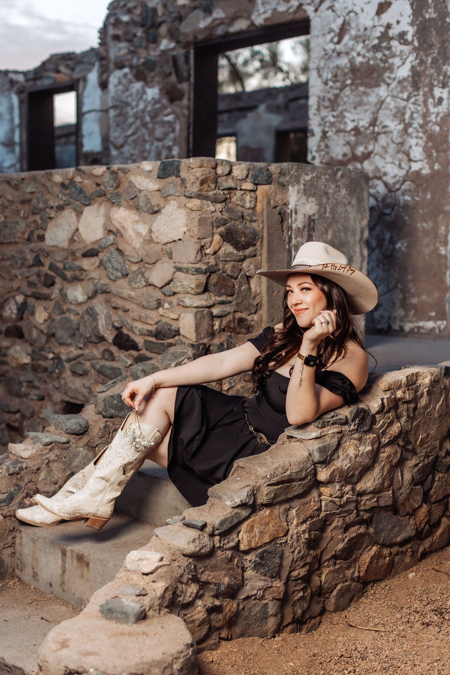 A western-style portrait showing someone in a wide-brimmed hat and boots relaxing on rustic stone steps.