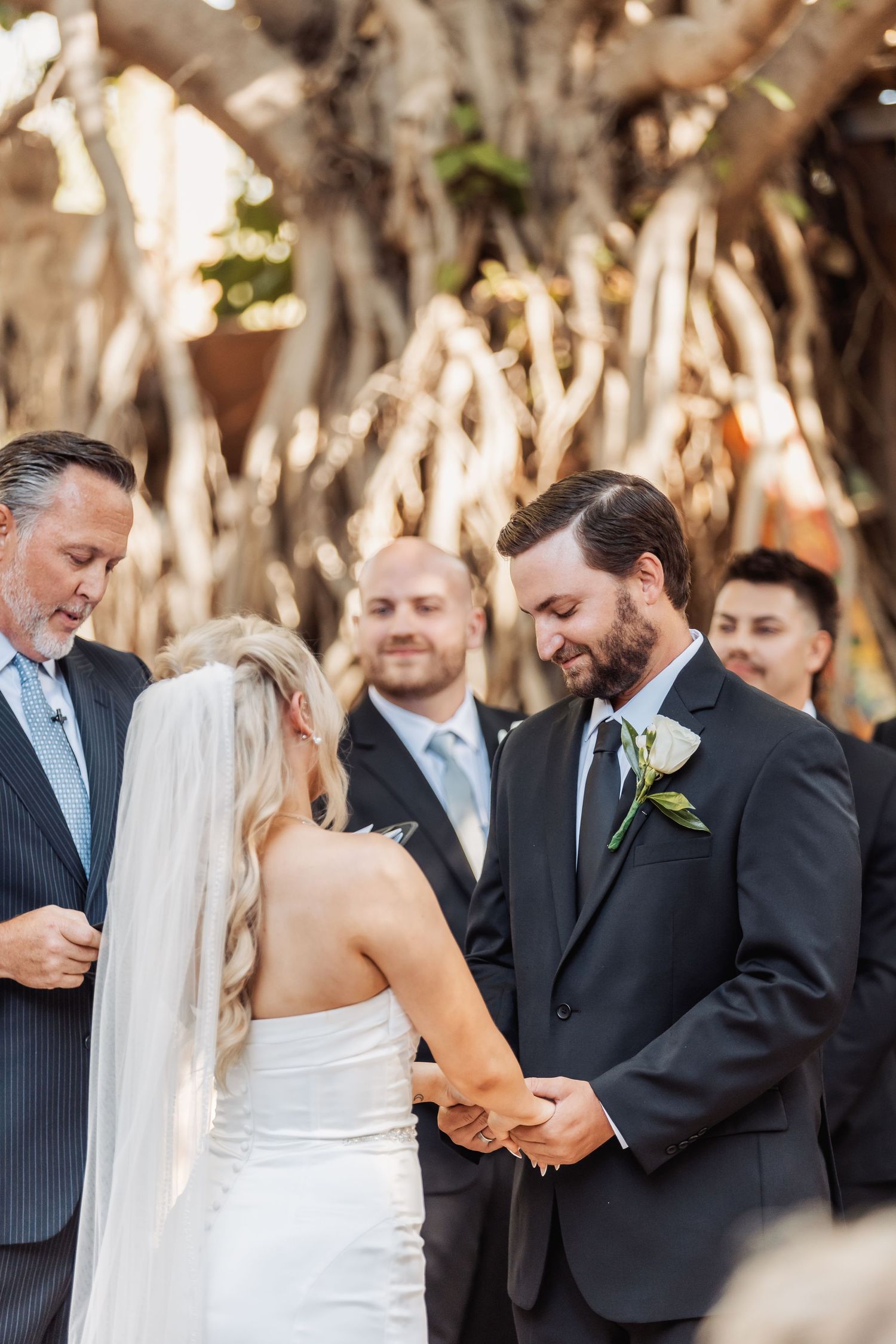 Intimate wedding ceremony moment captured under natural tree canopy with guests looking on.