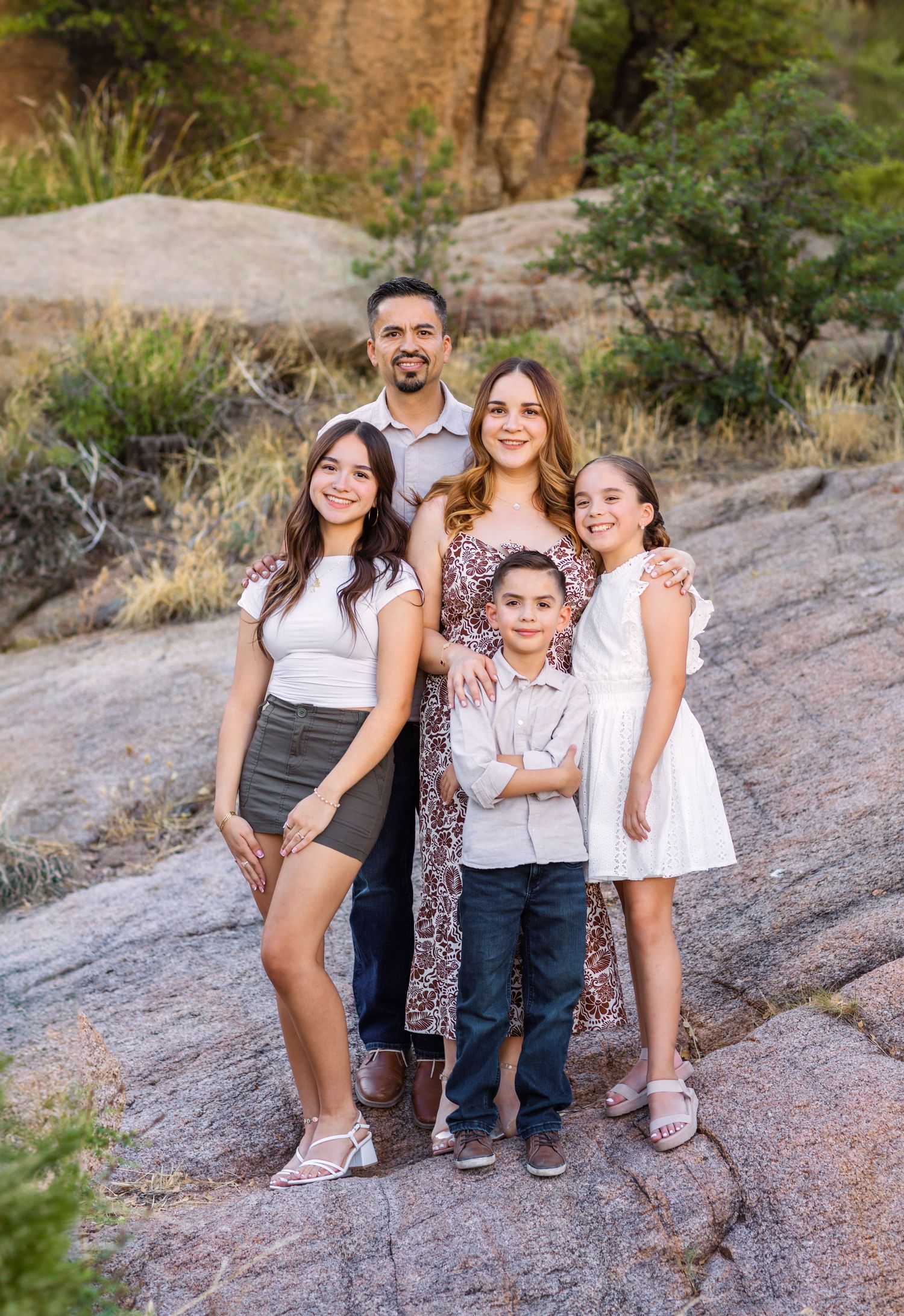 Family portrait session on rocky desert terrain during sunset showing playful poses and coordinated casual outfits.