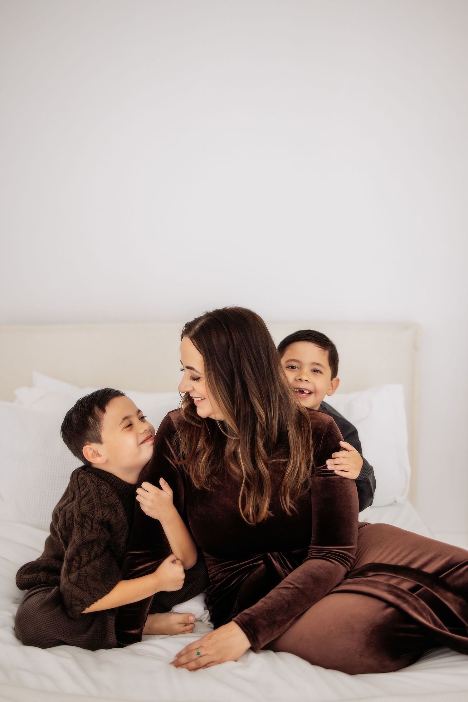 A heartwarming series of intimate moments between parent and child lying together in cozy brown sweaters on white bedding.