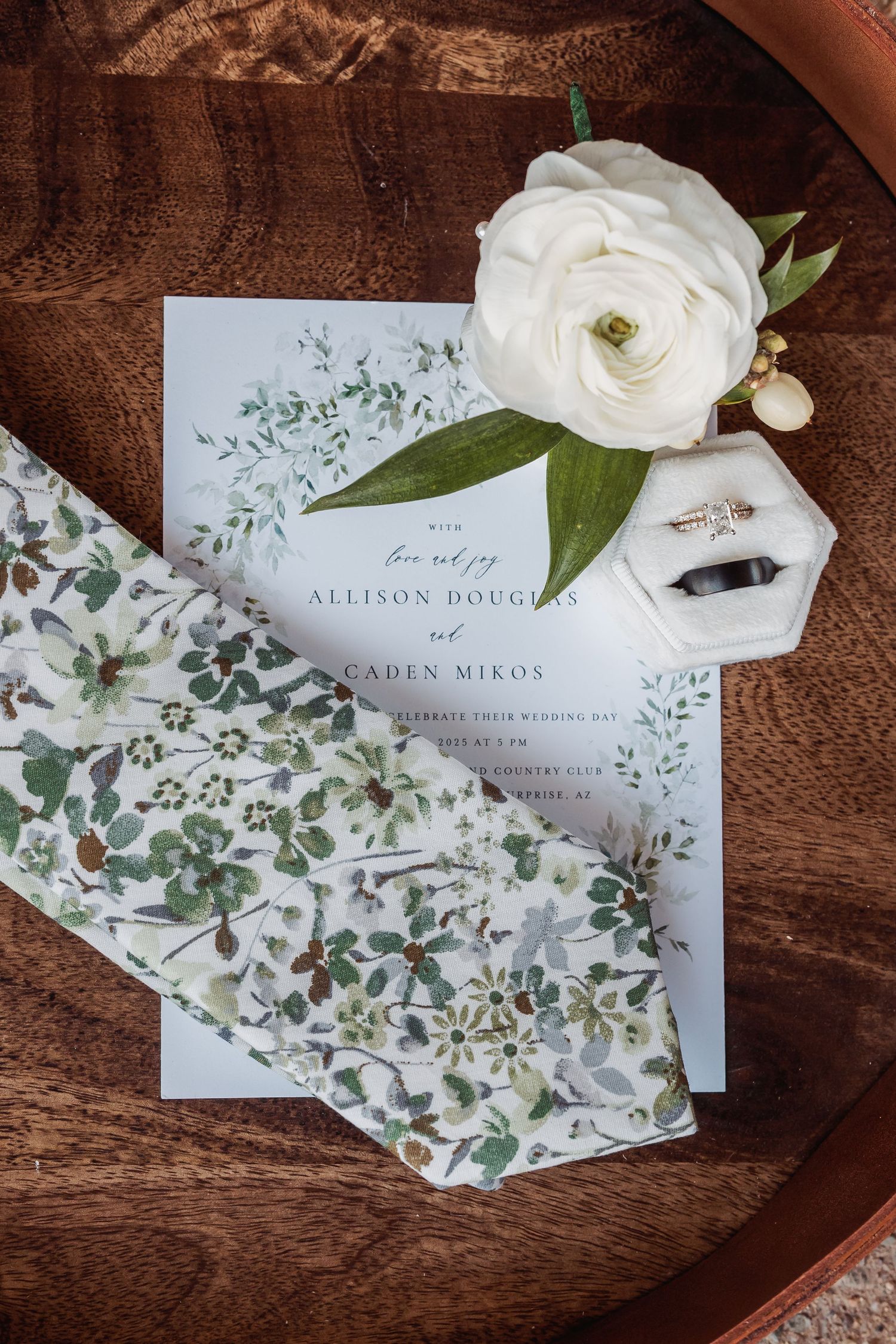Elegant wedding invitations with floral designs and greenery laid out on a wooden surface.