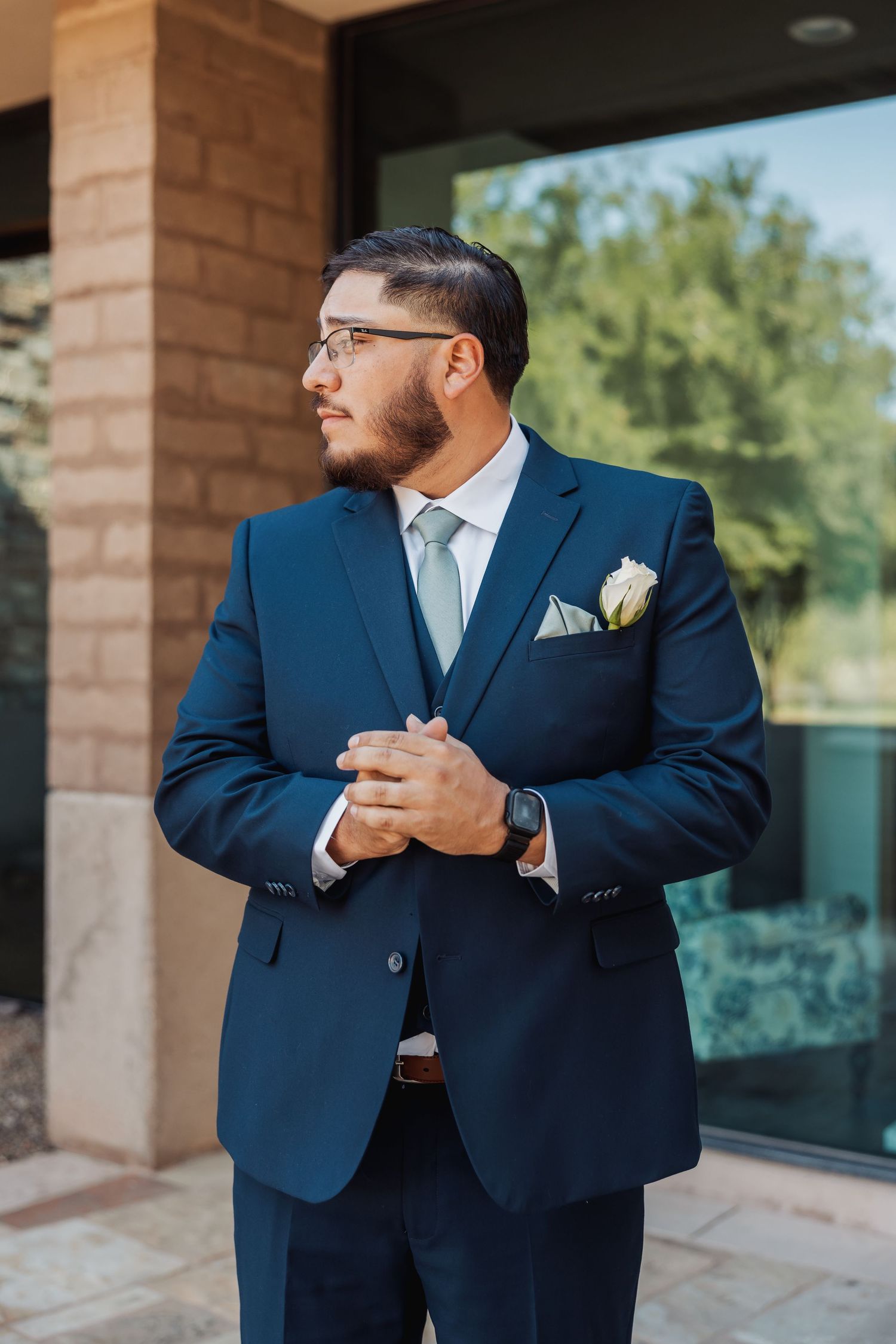 Two people in navy blue suits embrace in a warm hug on a patio with brick columns and greenery in background.