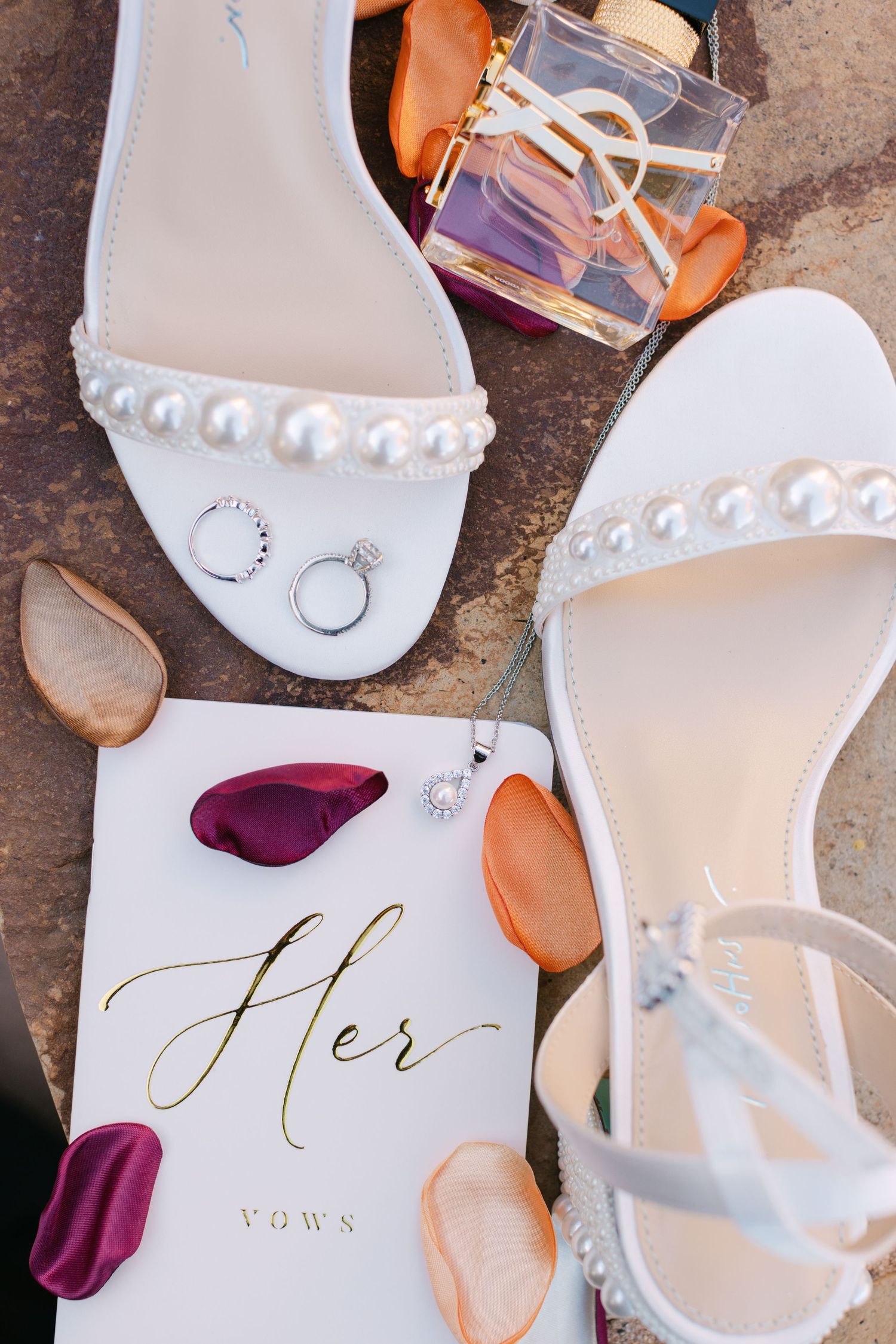 White bridal shoes with pearl details and gold calligraphy text displayed alongside burgundy flower petals.