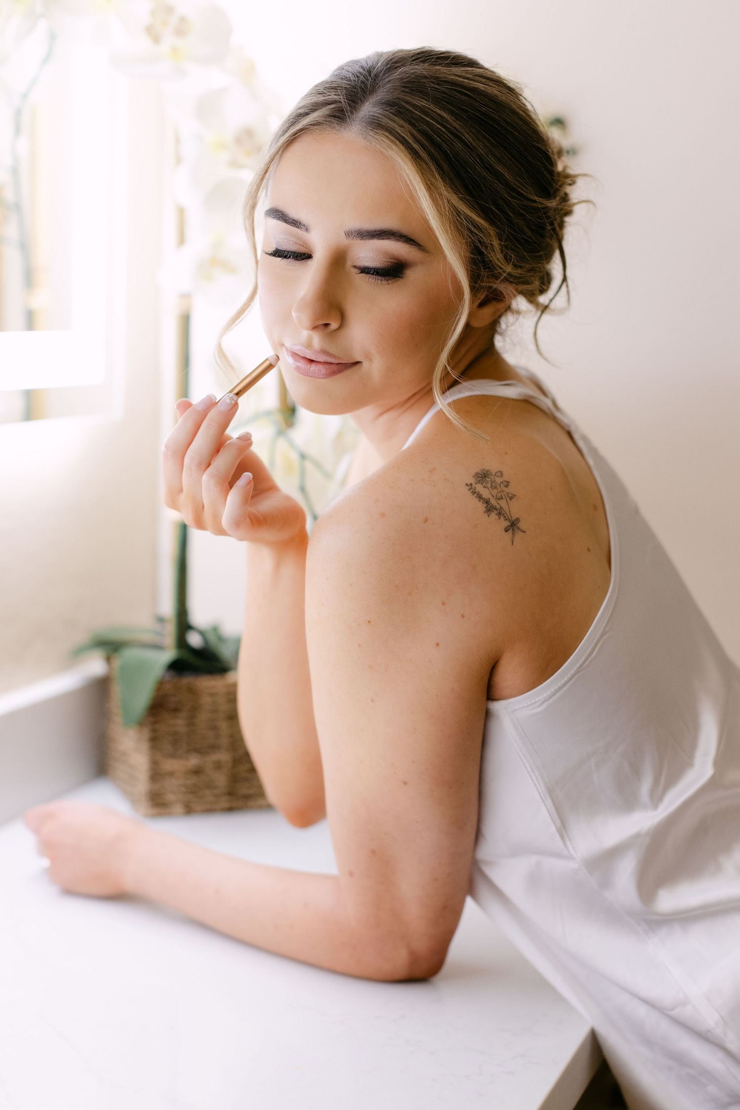 A bride in white resting on white bedding during a quiet moment of wedding day preparation.