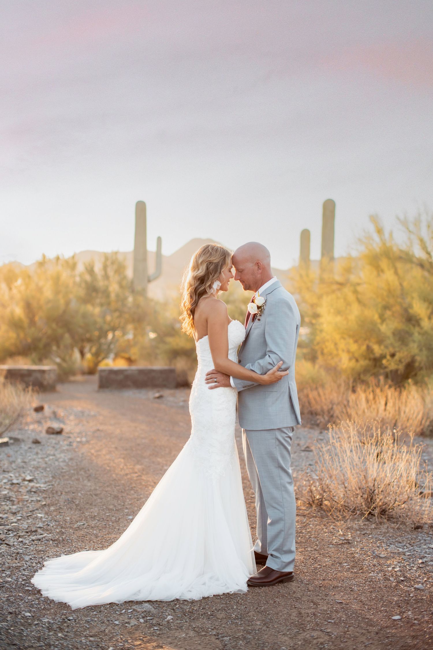 A couple shares romantic moments at sunset in a desert landscape with towering saguaro cacti in the background.