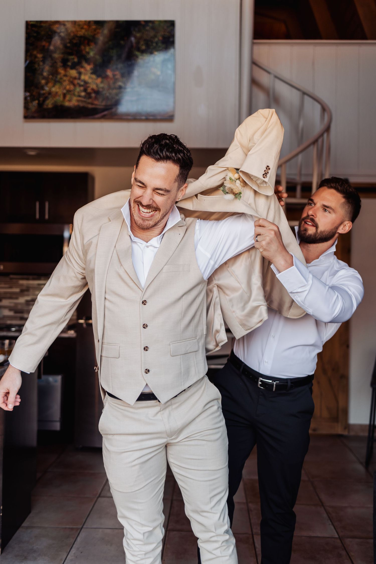 Playful groomsmen in light colored suits dancing and celebrating indoors.