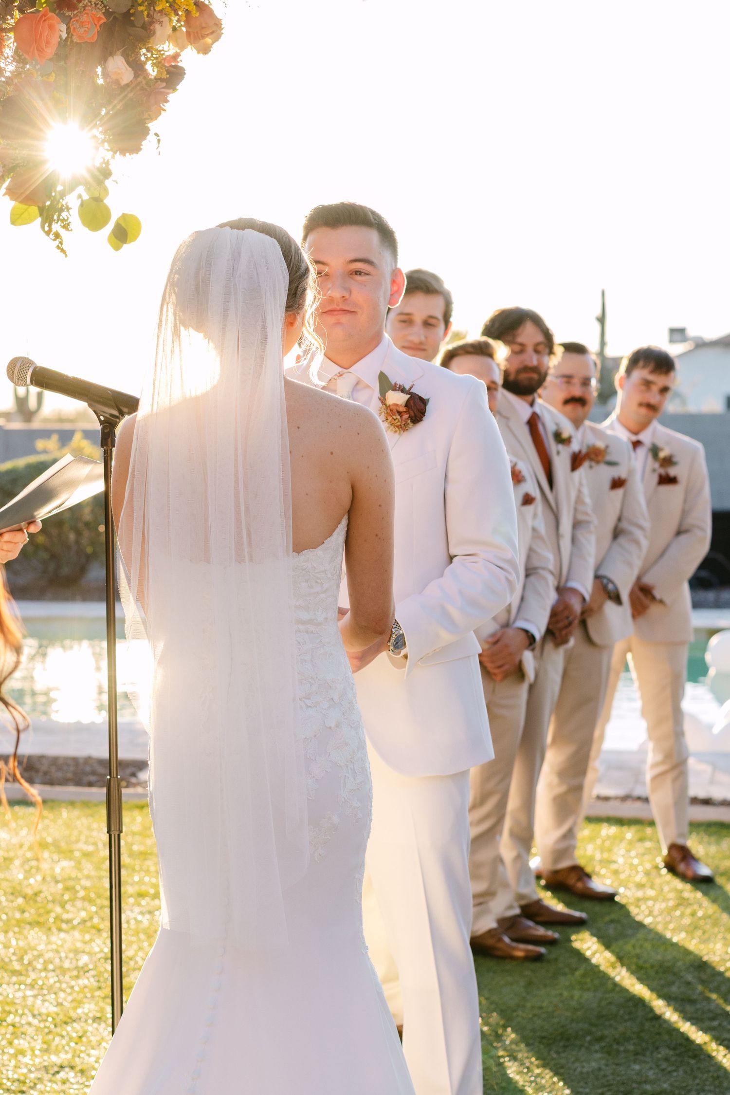 A wedding party in white and beige attire poses together outdoors during golden hour sunset.