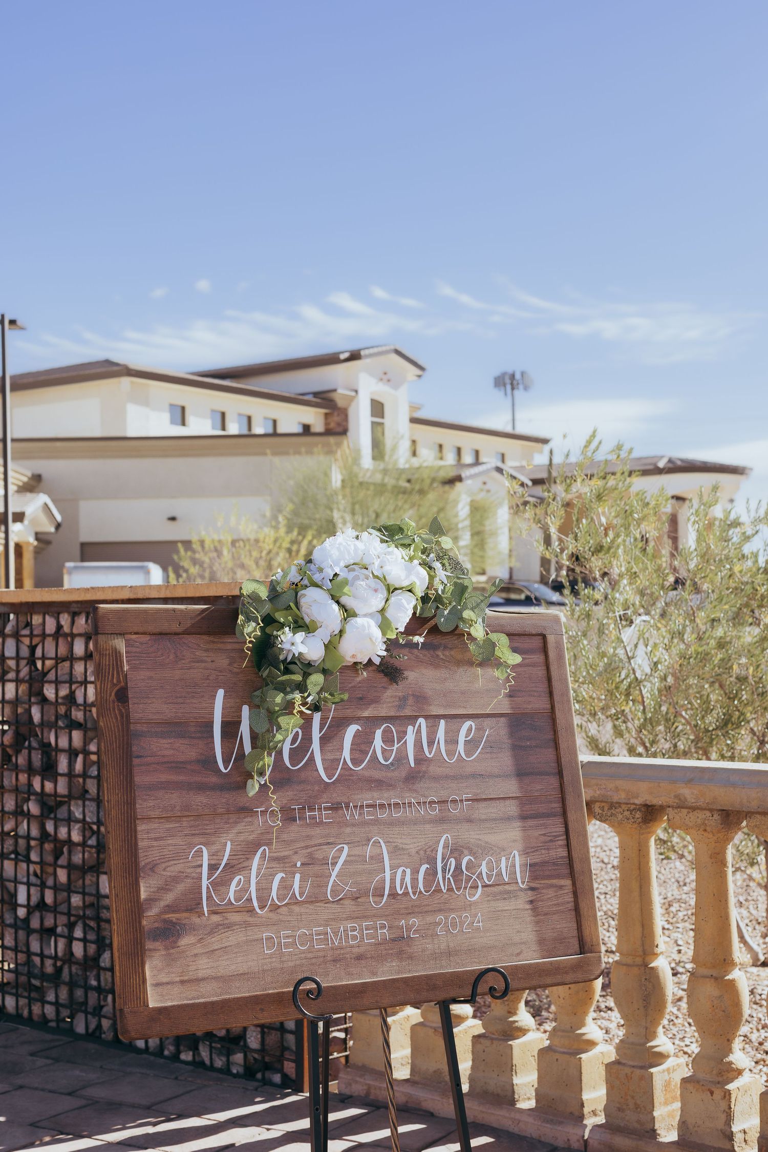 Wooden welcome signs with elegant calligraphy displayed on stone balustrades at an outdoor wedding venue.