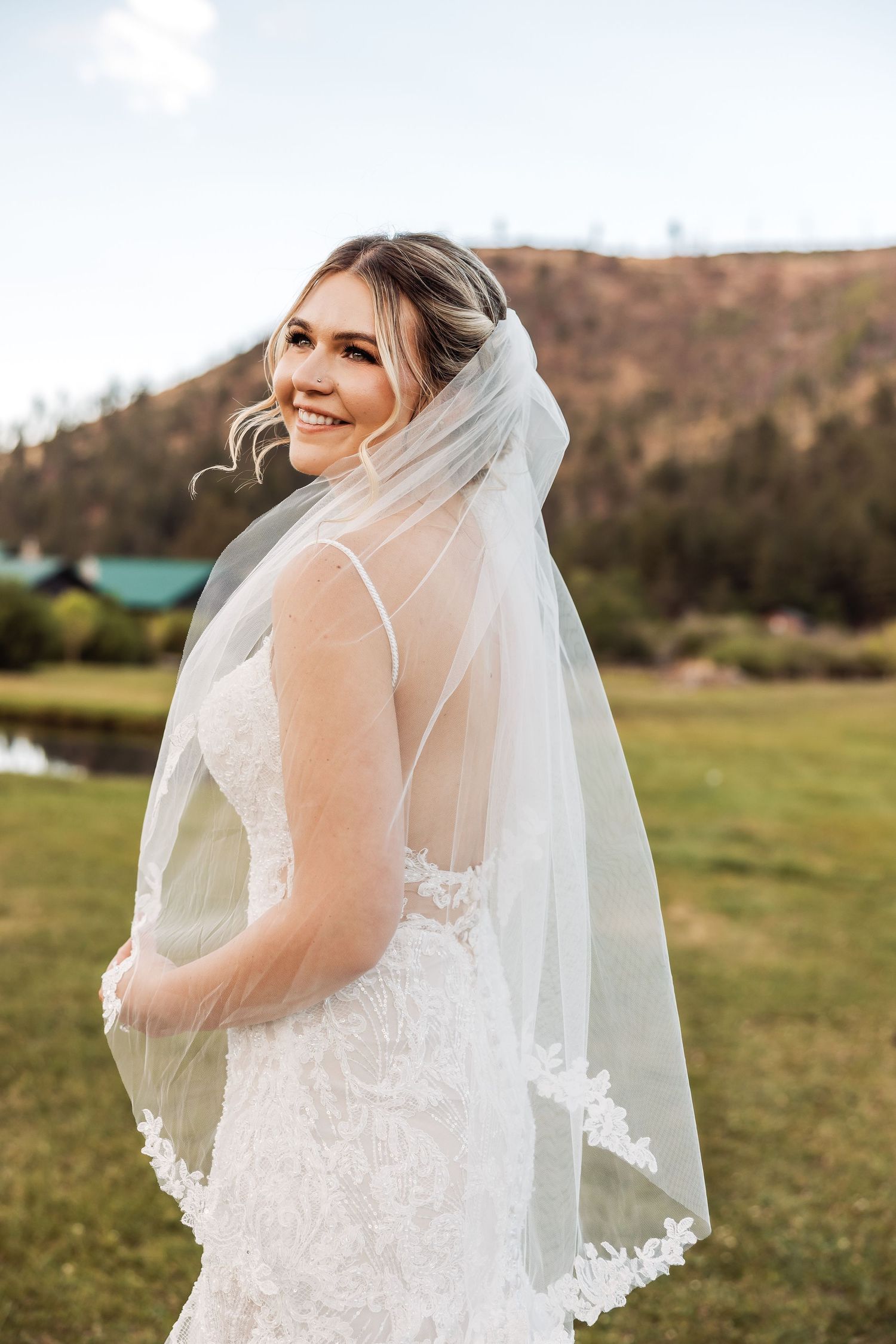 A flowing white bridal veil with delicate lace detailing blows in the wind against a scenic mountain backdrop.
