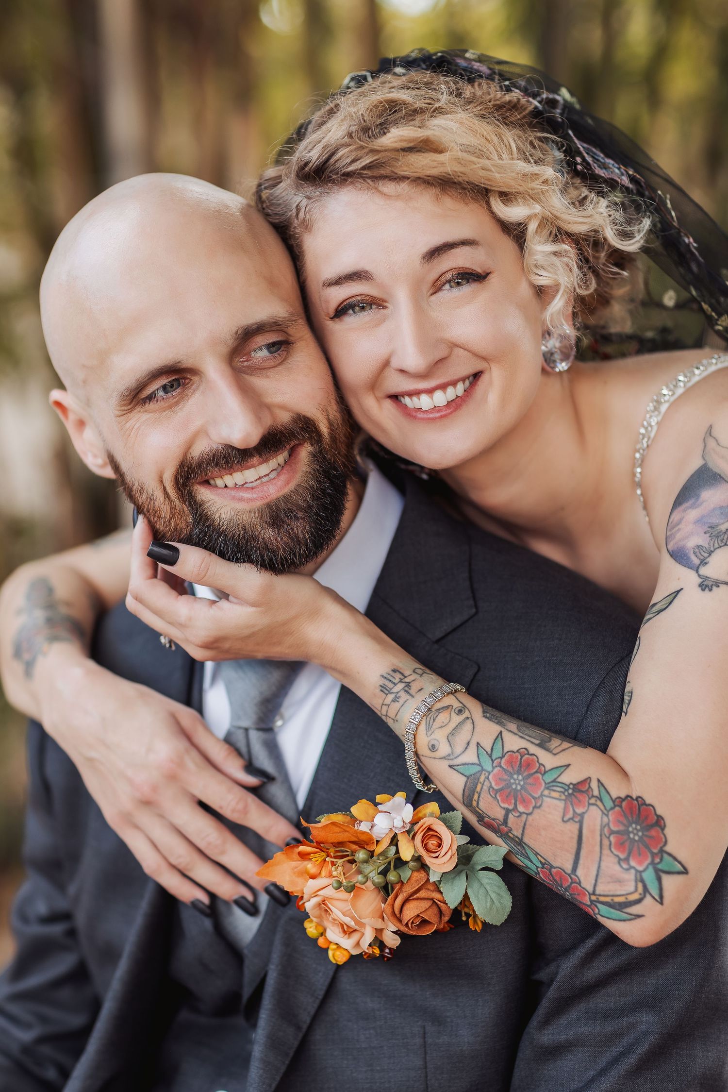A joyful wedding portrait featuring colorful orange florals and artistic tattoos against a forest backdrop.