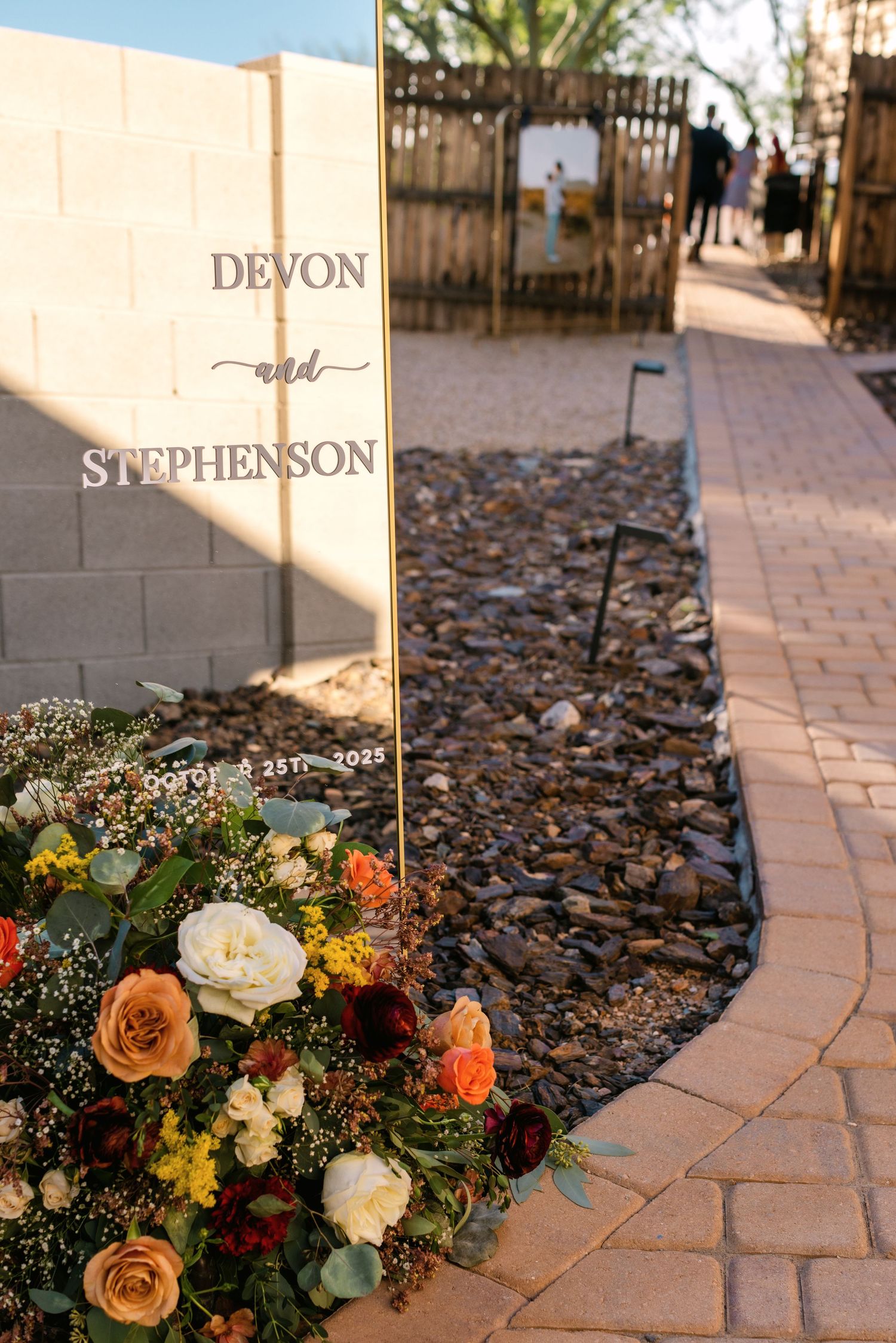 Stone pathway lined with mulch and decorated with autumn floral arrangements next to name markers at an outdoor venue.