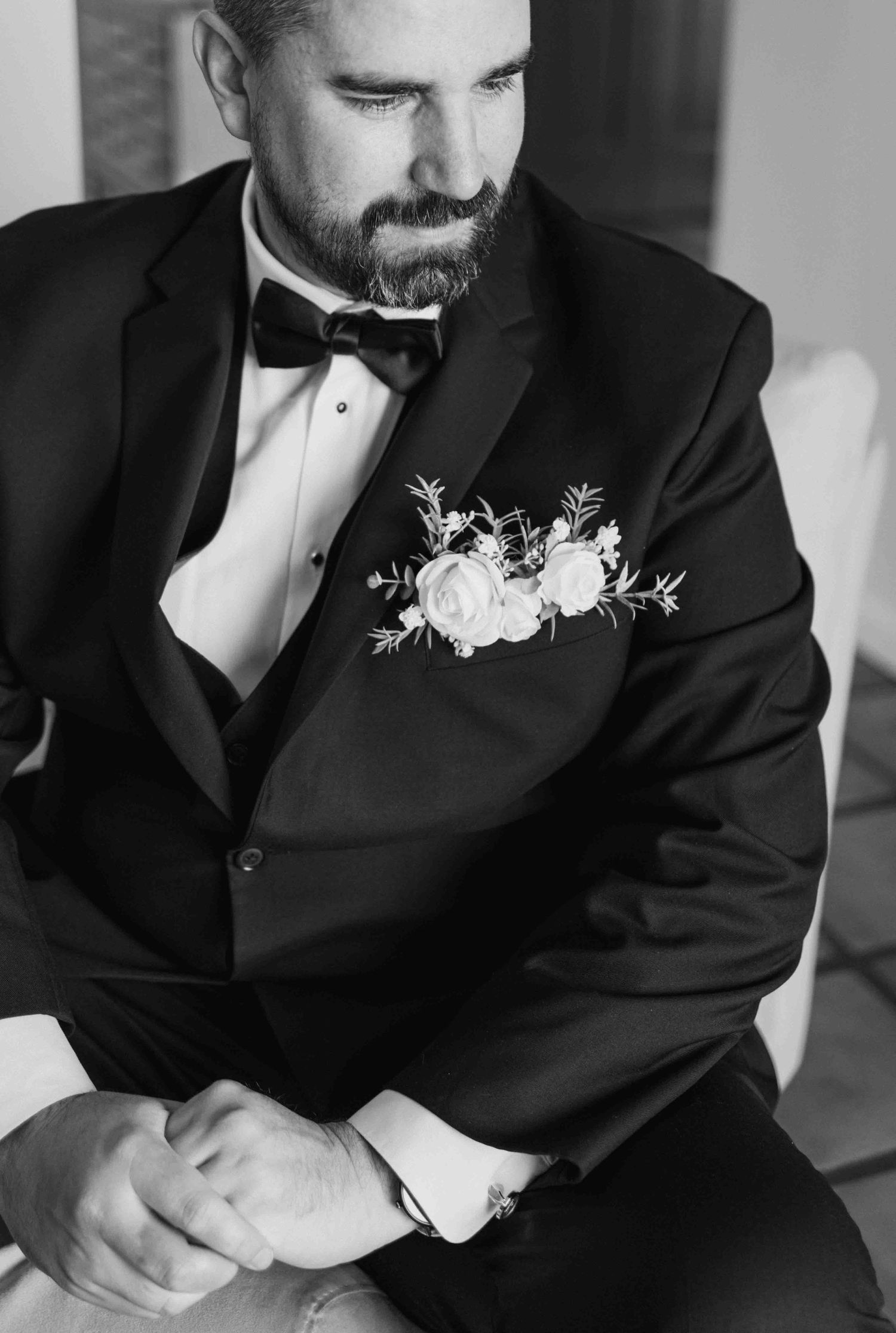 Close-up black and white photo of groom in tuxedo with white boutonniere showing details of formal wedding attire.