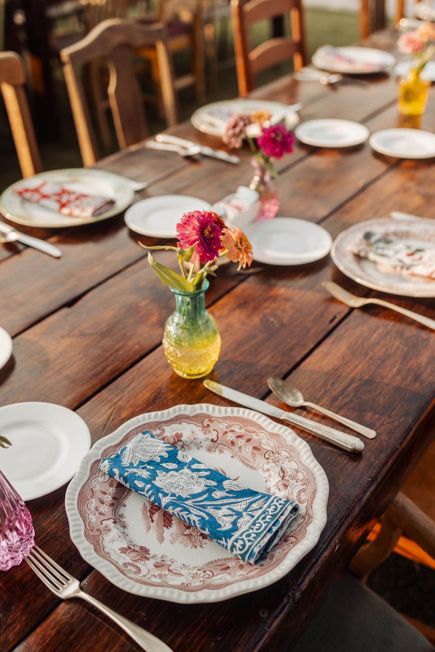 Rustic wedding table setting with vintage plates and colorful floral centerpieces.