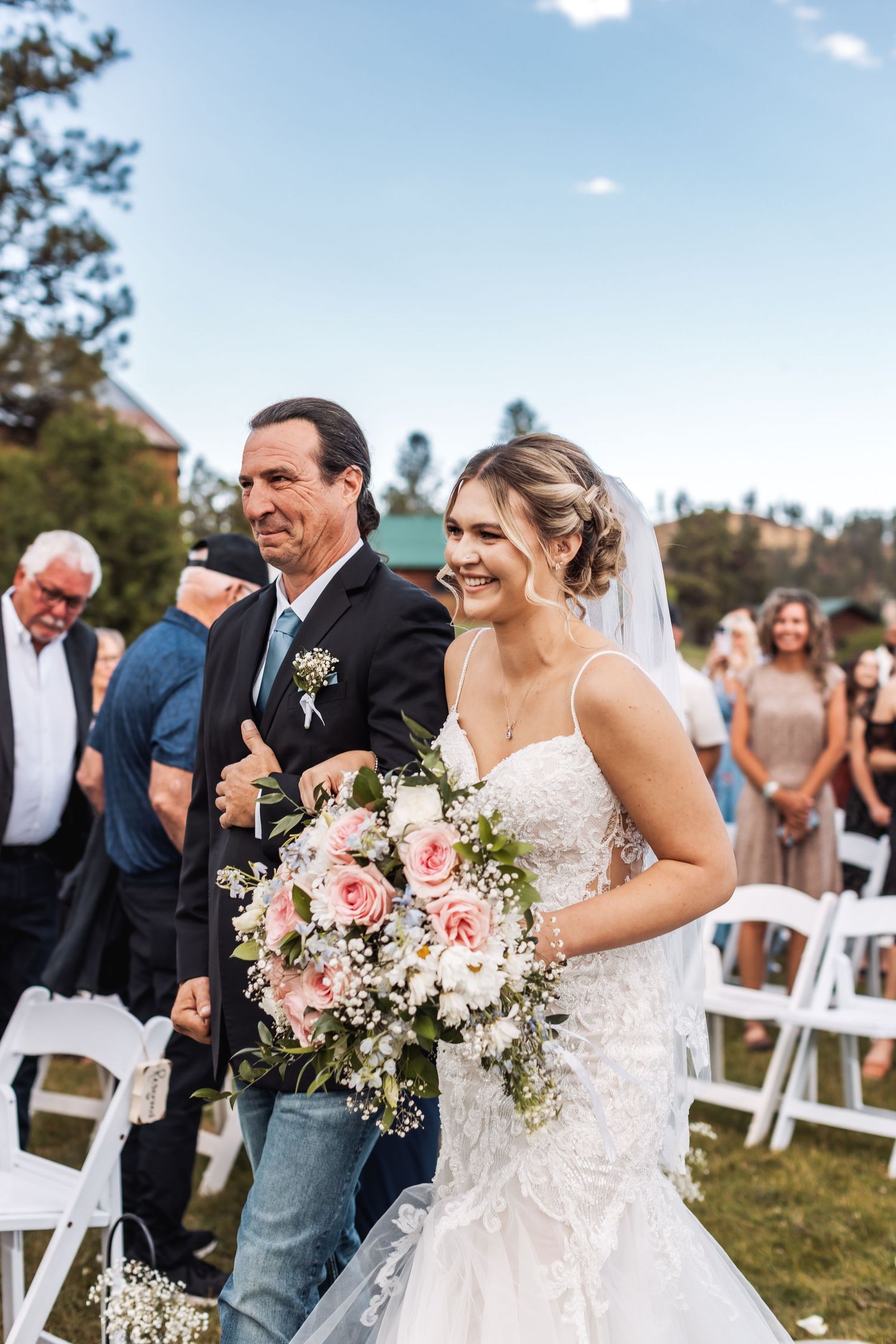 A joyful outdoor wedding ceremony with guests seated on white chairs and a couple sharing laughter.