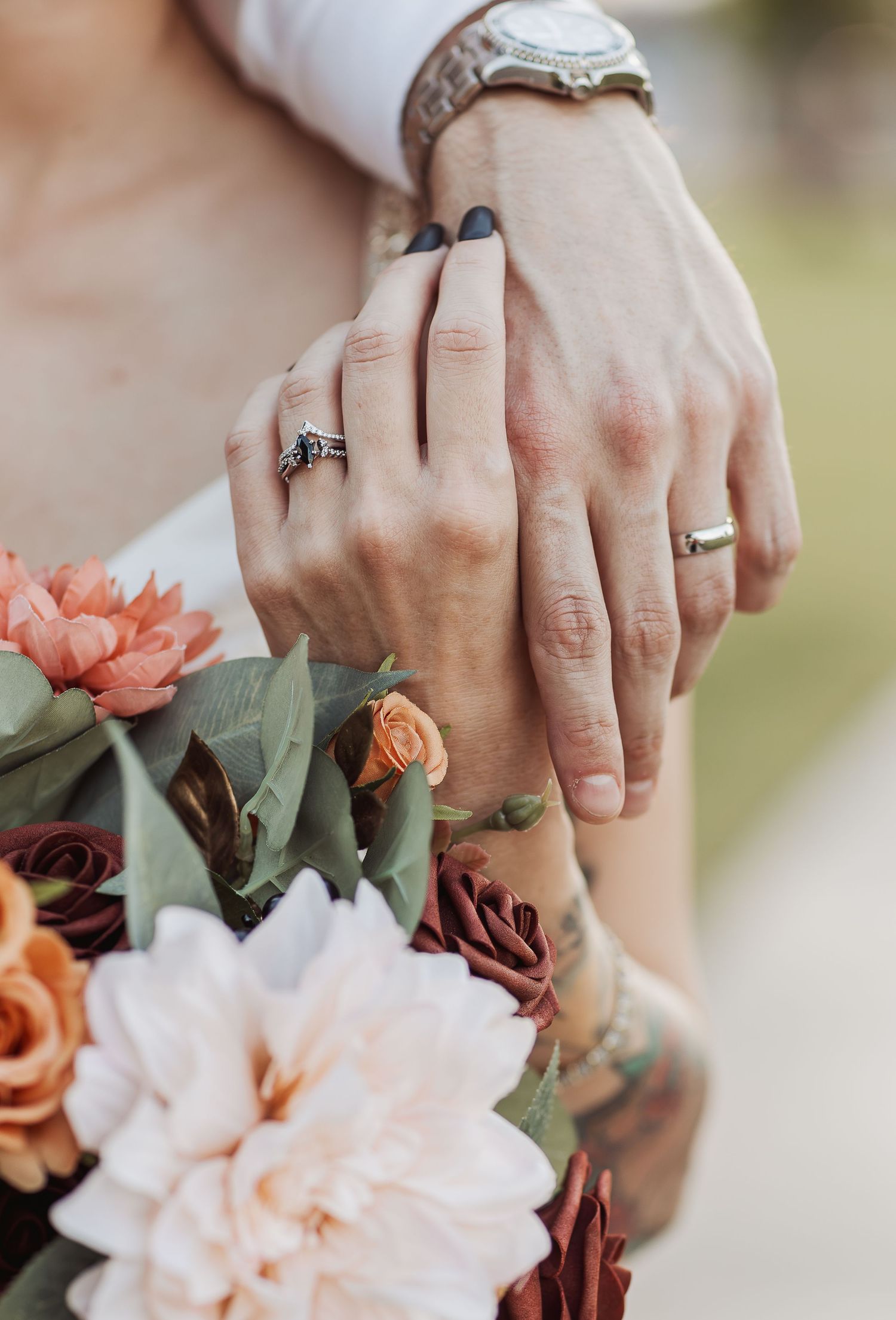 Close-up shots of hands wearing engagement rings holding delicate peach and white flowers in a romantic wedding detail.