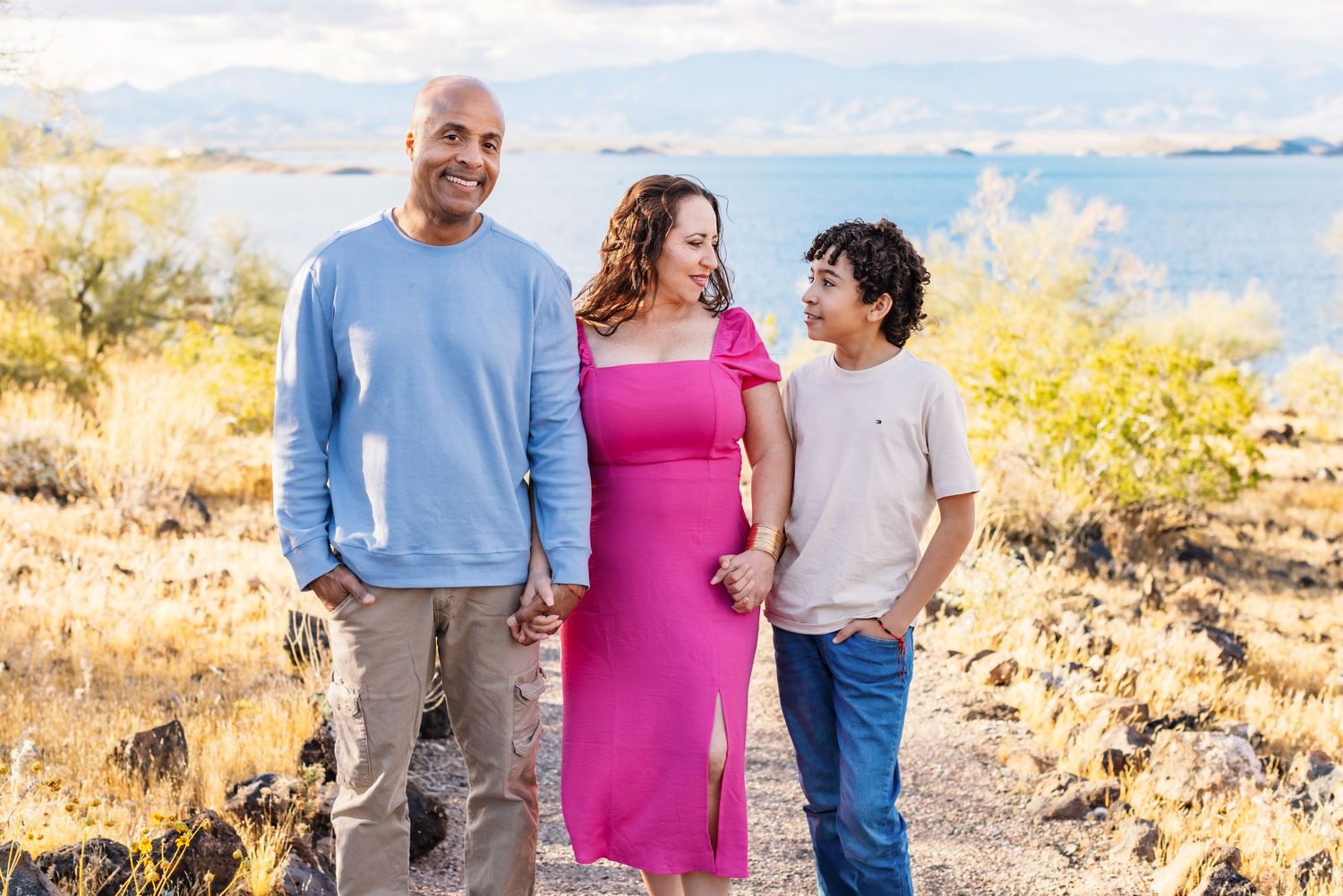 A couple and a child walking together on a scenic coastal path with ocean views and autumn foliage.
