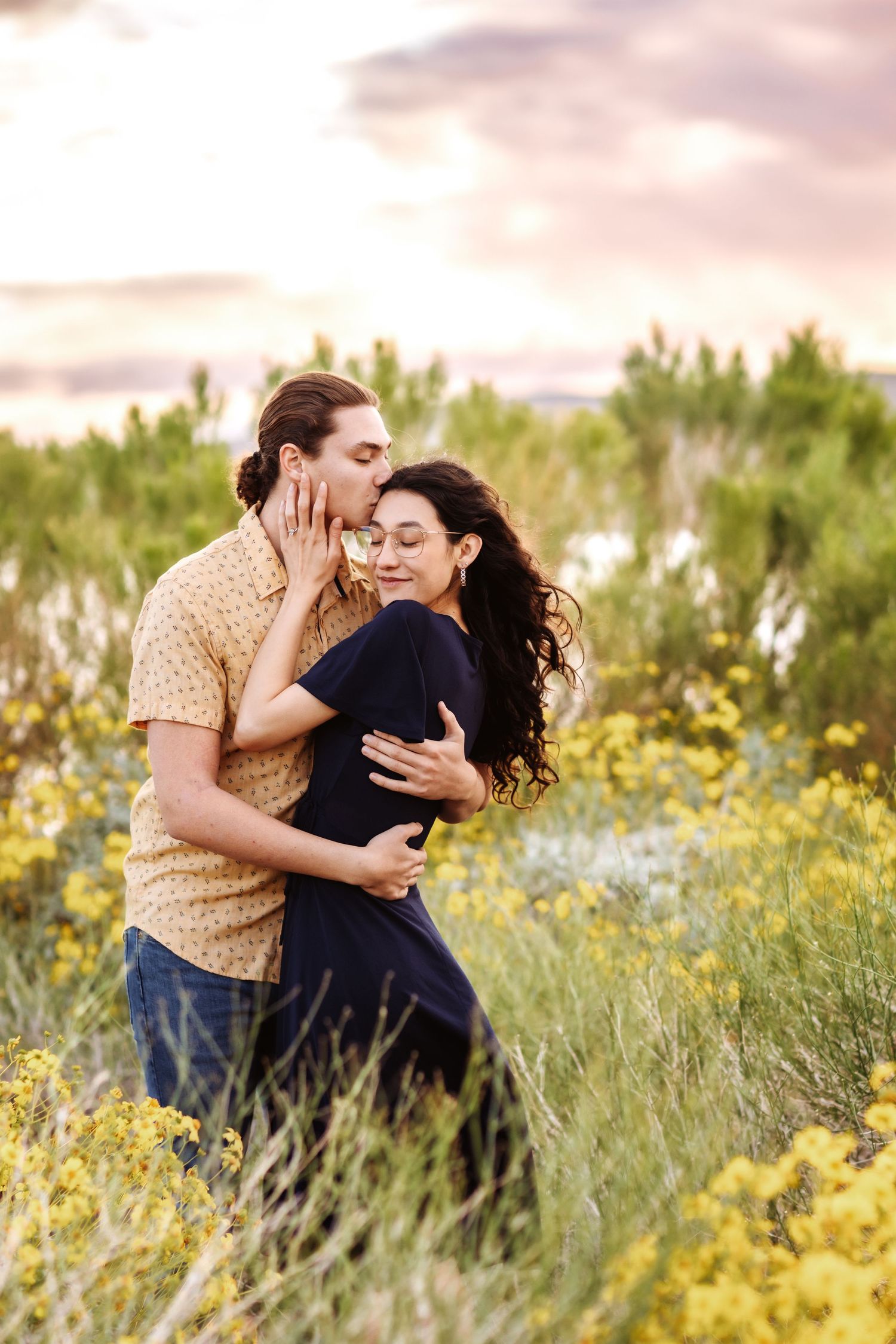 Romantic couple embraces in a field of yellow wildflowers during golden hour sunset.