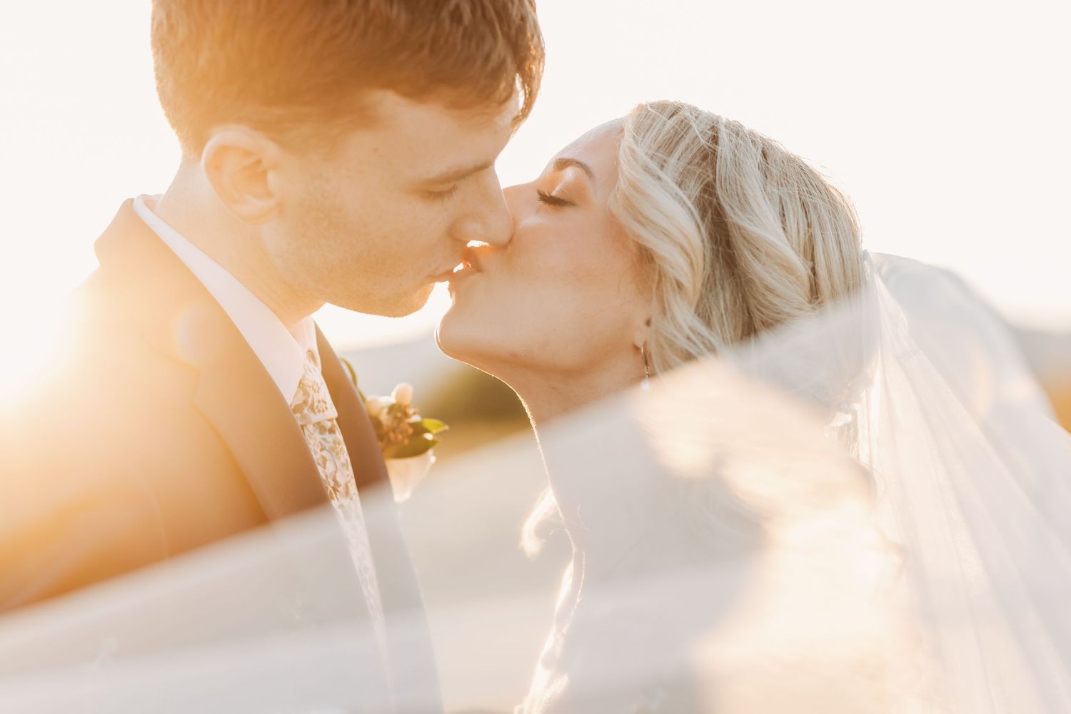 A romantic couple embraces under a sheer veil during an outdoor wedding photoshoot at golden hour.