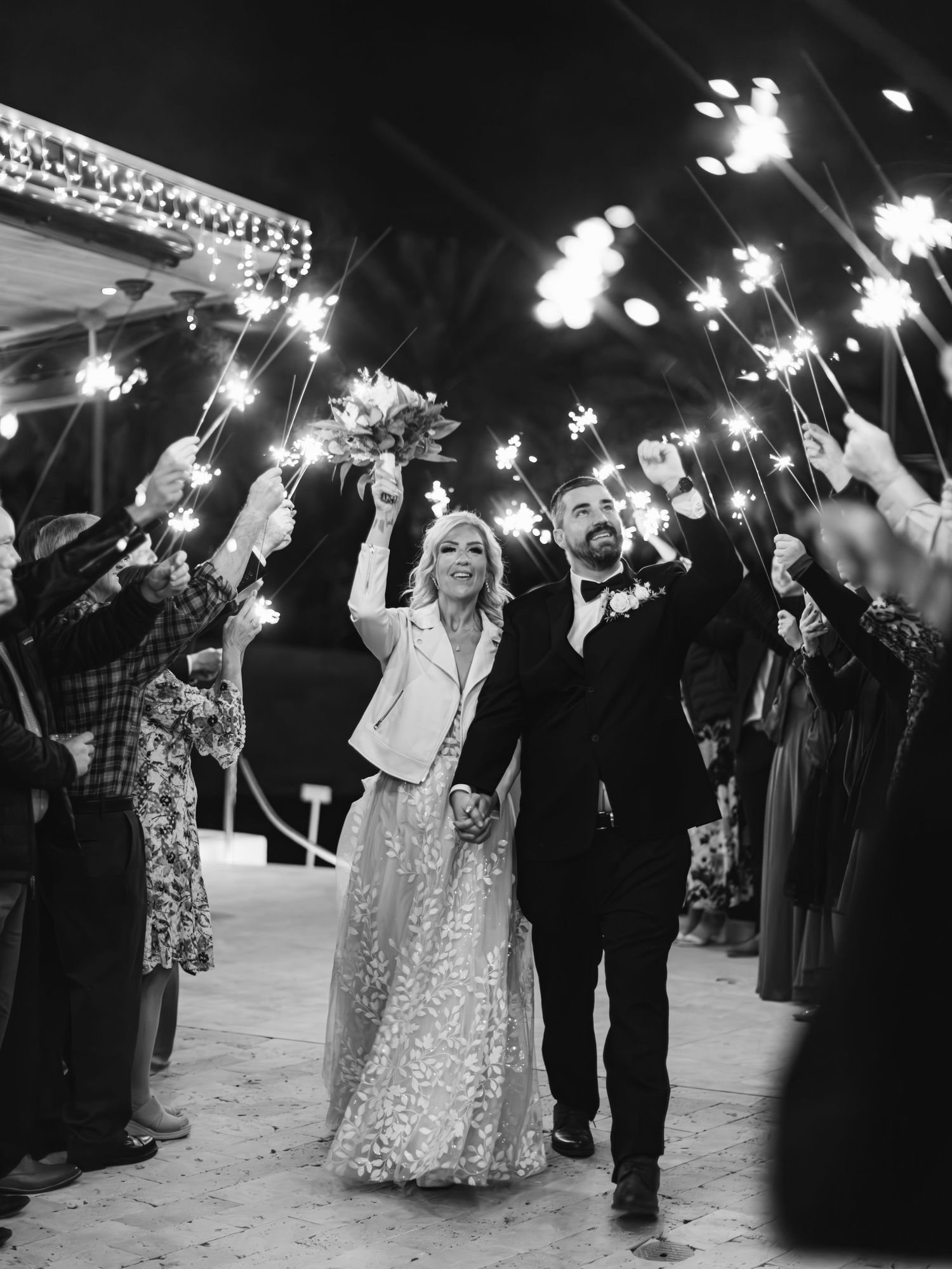 Wedding guests hold sparklers during a nighttime send-off celebration creating a magical illuminated walkway.