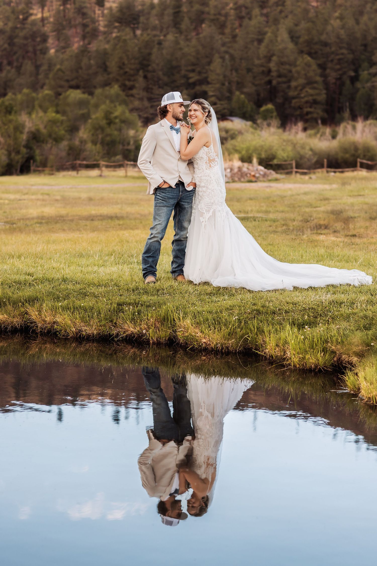 A romantic wedding photo with reflections in a pond against a mountain backdrop and forest scenery.