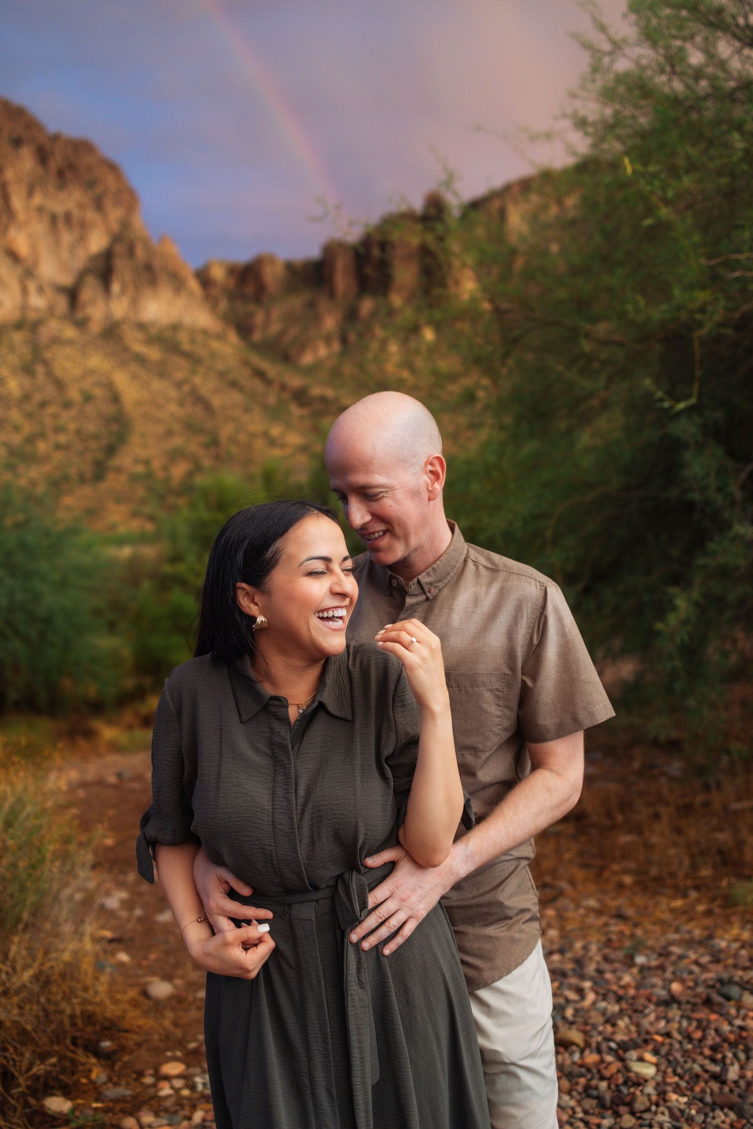 A couple shares a joyful moment together against the backdrop of rugged desert mountains at sunset.