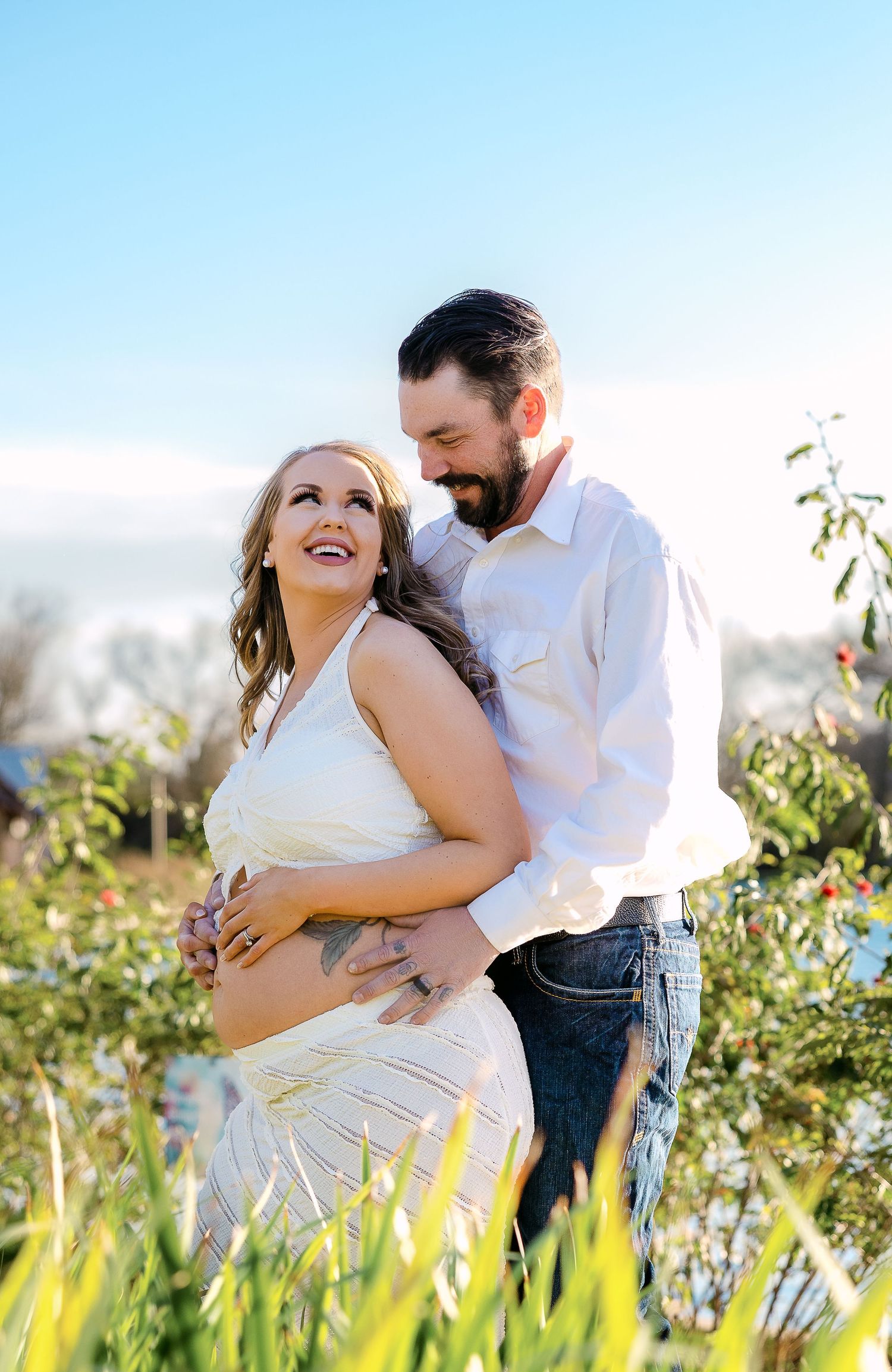 Romantic maternity photoshoot of a couple embracing in a sunlit meadow with wildflowers.