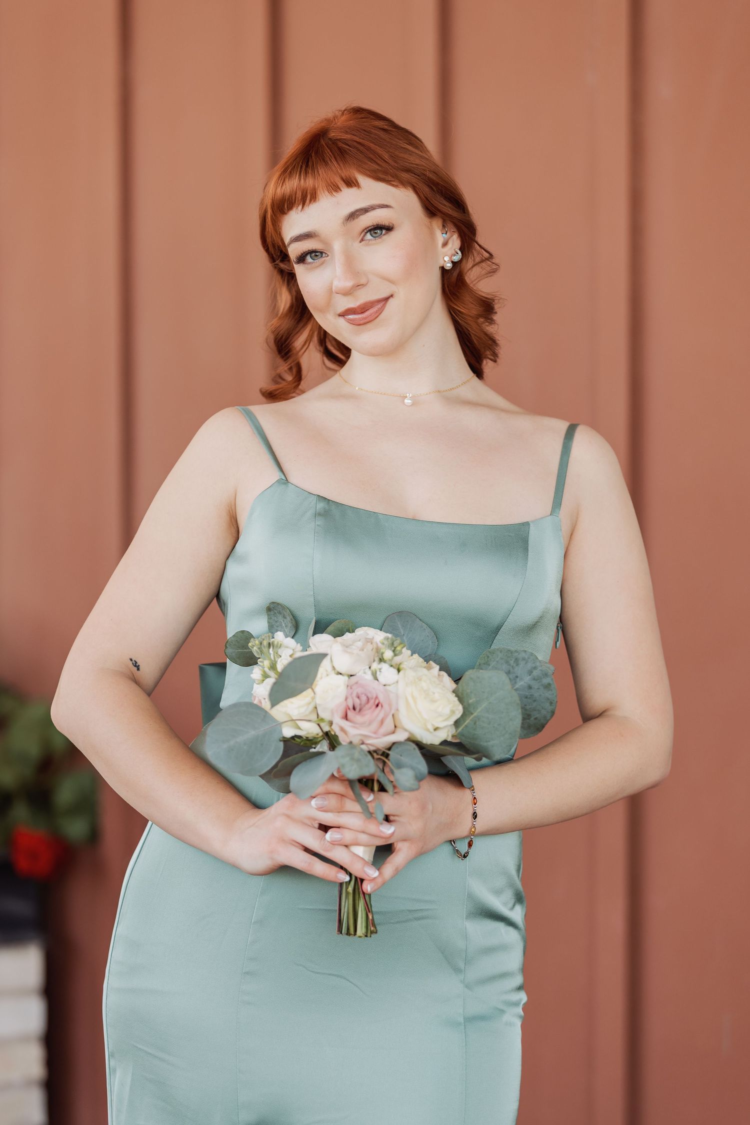 Bridesmaid in sage green satin dress holding a delicate bouquet of white and pink roses.