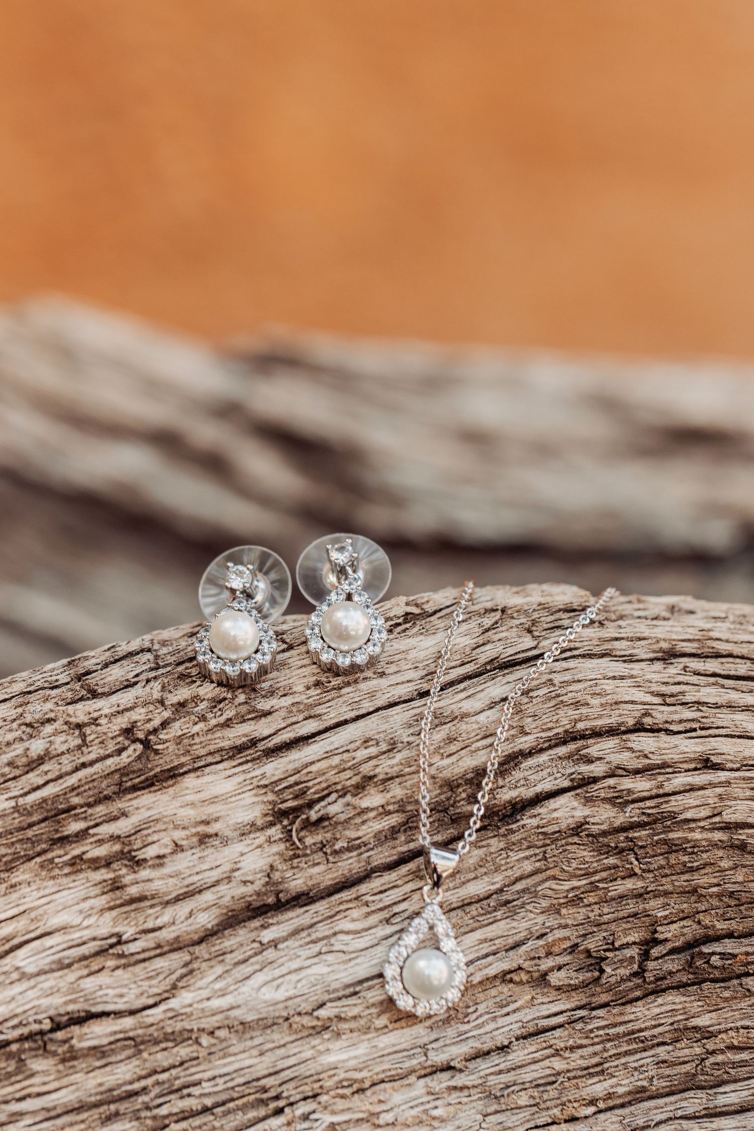Diamond stud earrings displayed on rustic weathered driftwood against an orange-tinted background.