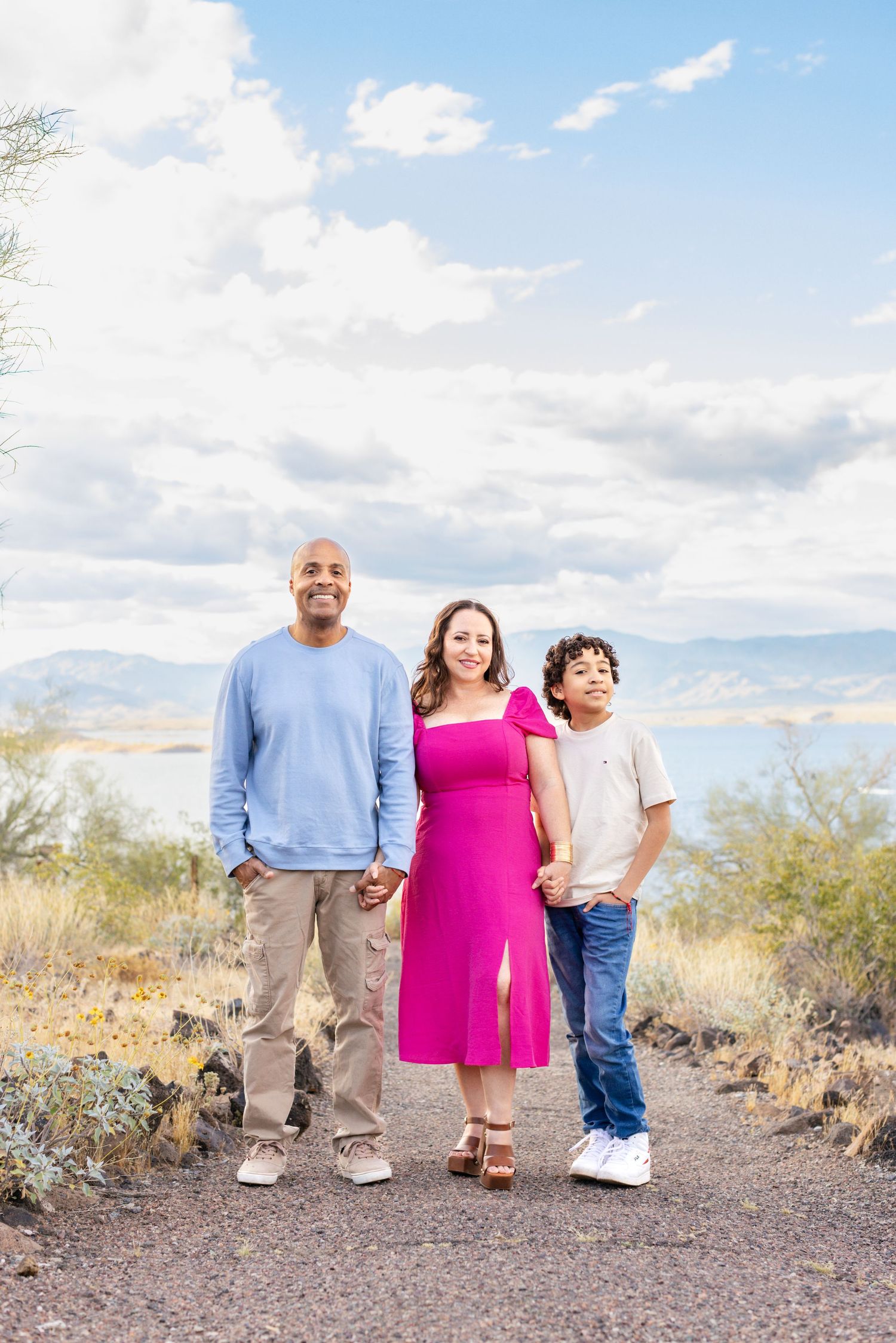 A family stands together on a desert trail with mountains and blue sky in the background.